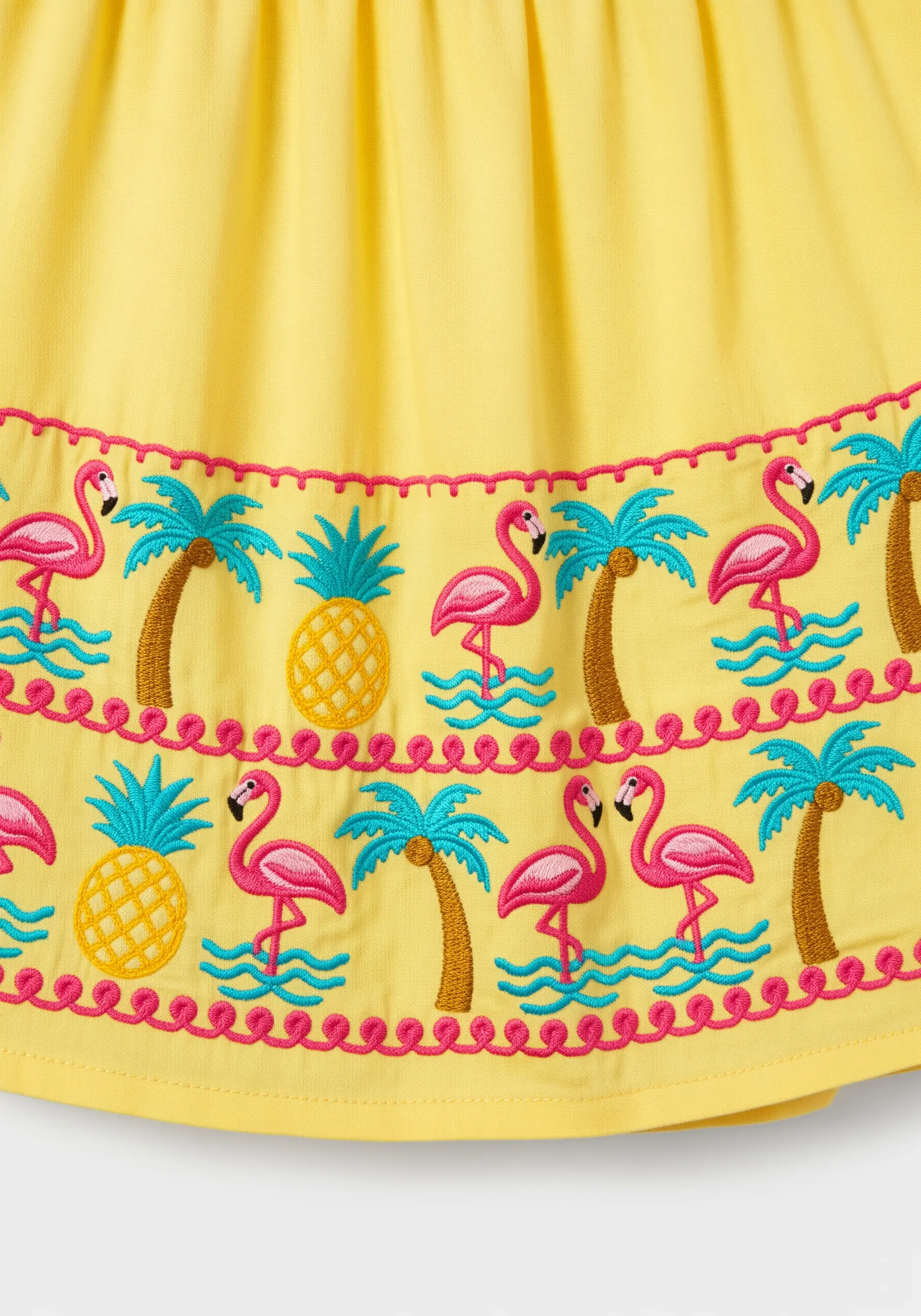 Repeating flamingo and palm tree border embroidery on yellow fabric