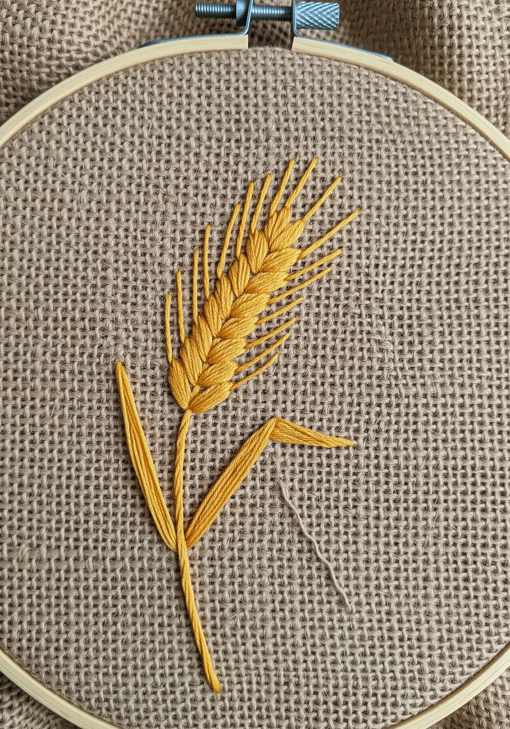 A golden yellow wheat stalk embroidered on coarse brown burlap fabric.
