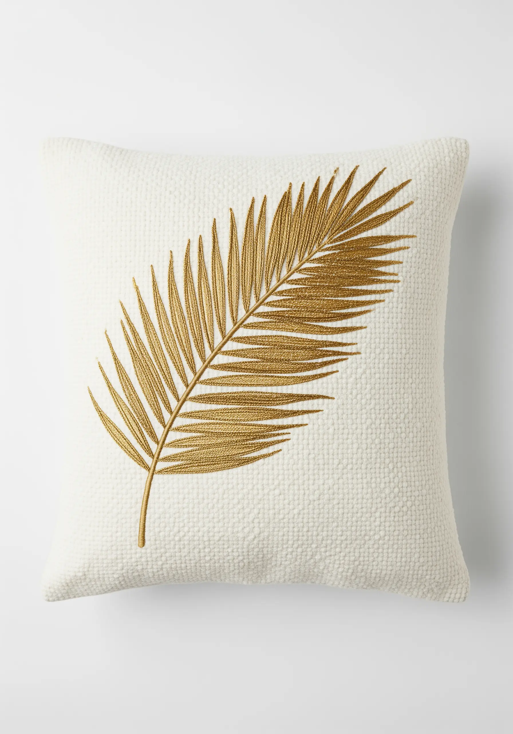 Gold satin stitch palm leaf on a textured white bouclé cushion.