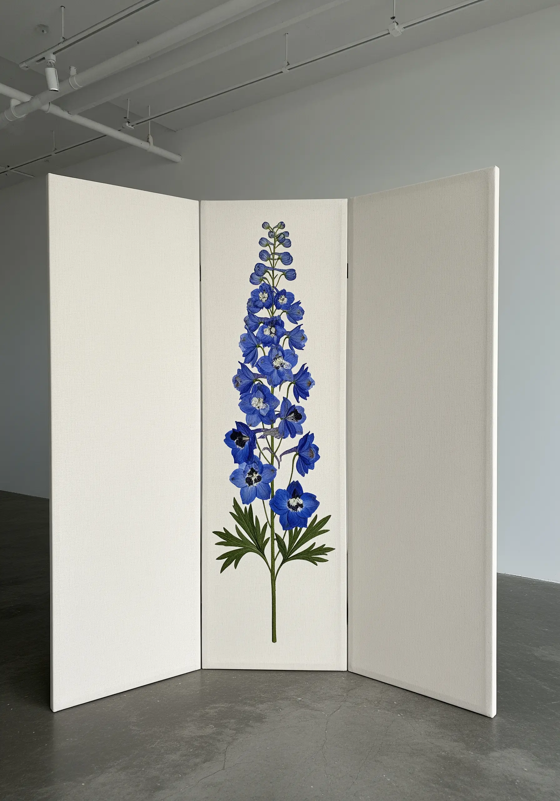 A large-scale embroidery of a blue delphinium on the central panel of a white room divider.