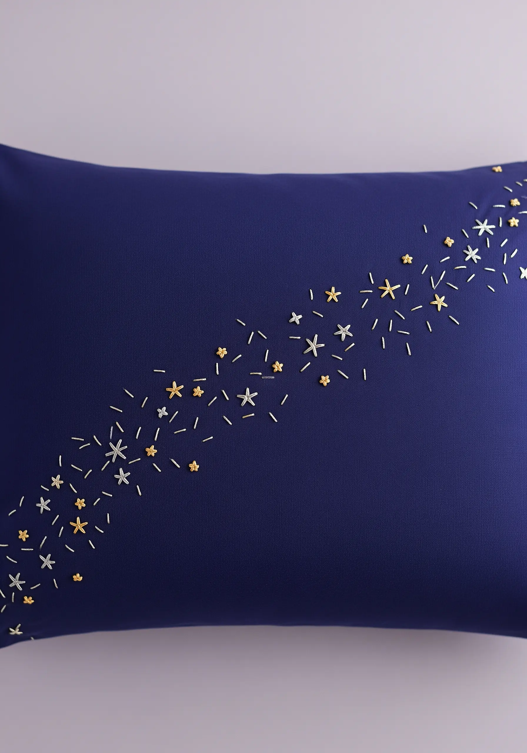 A diagonal scatter of embroidered gold and silver stars and seed stitches on a navy blue pillowcase.