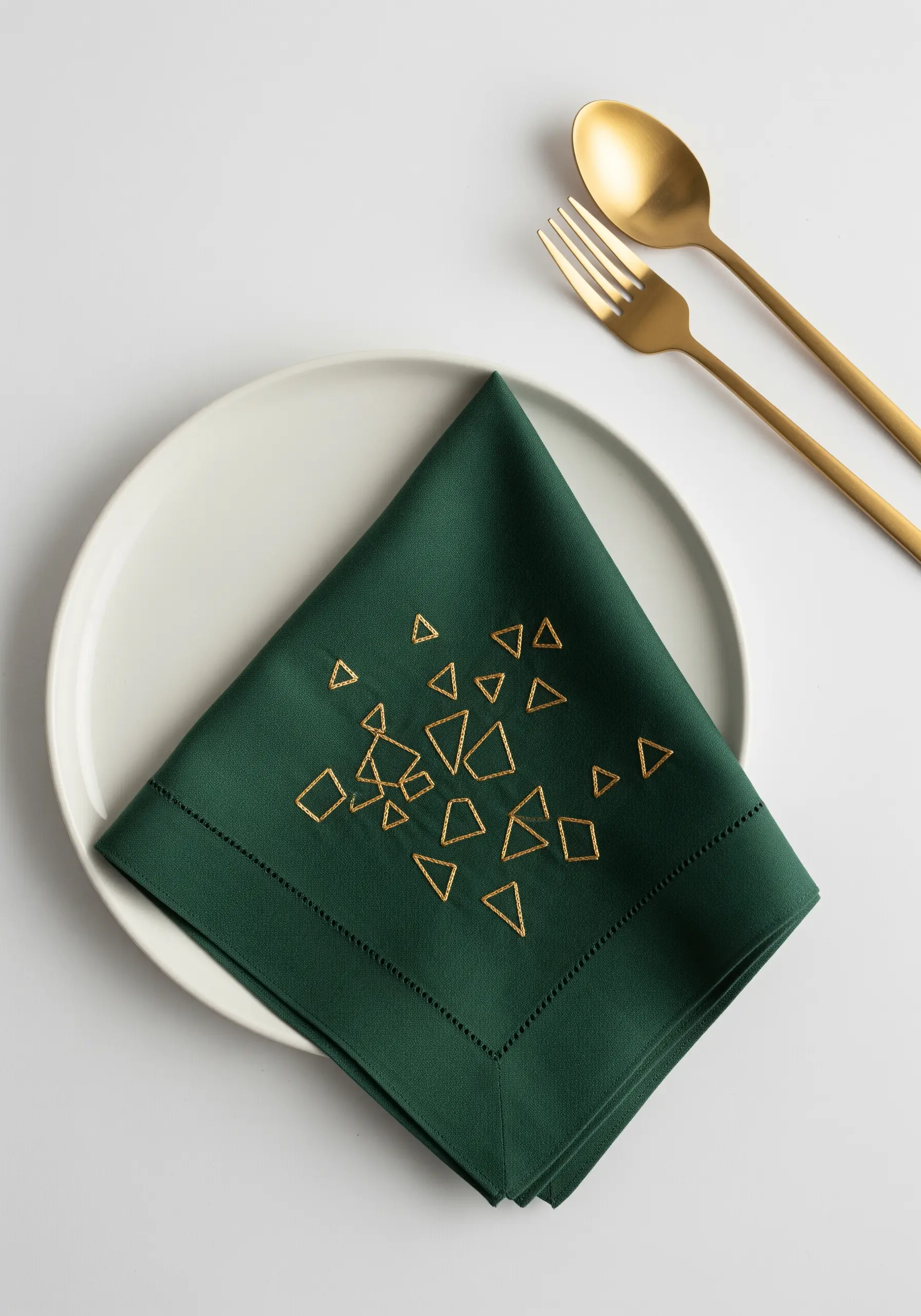 Gold metallic thread triangles embroidered on a dark green linen napkin