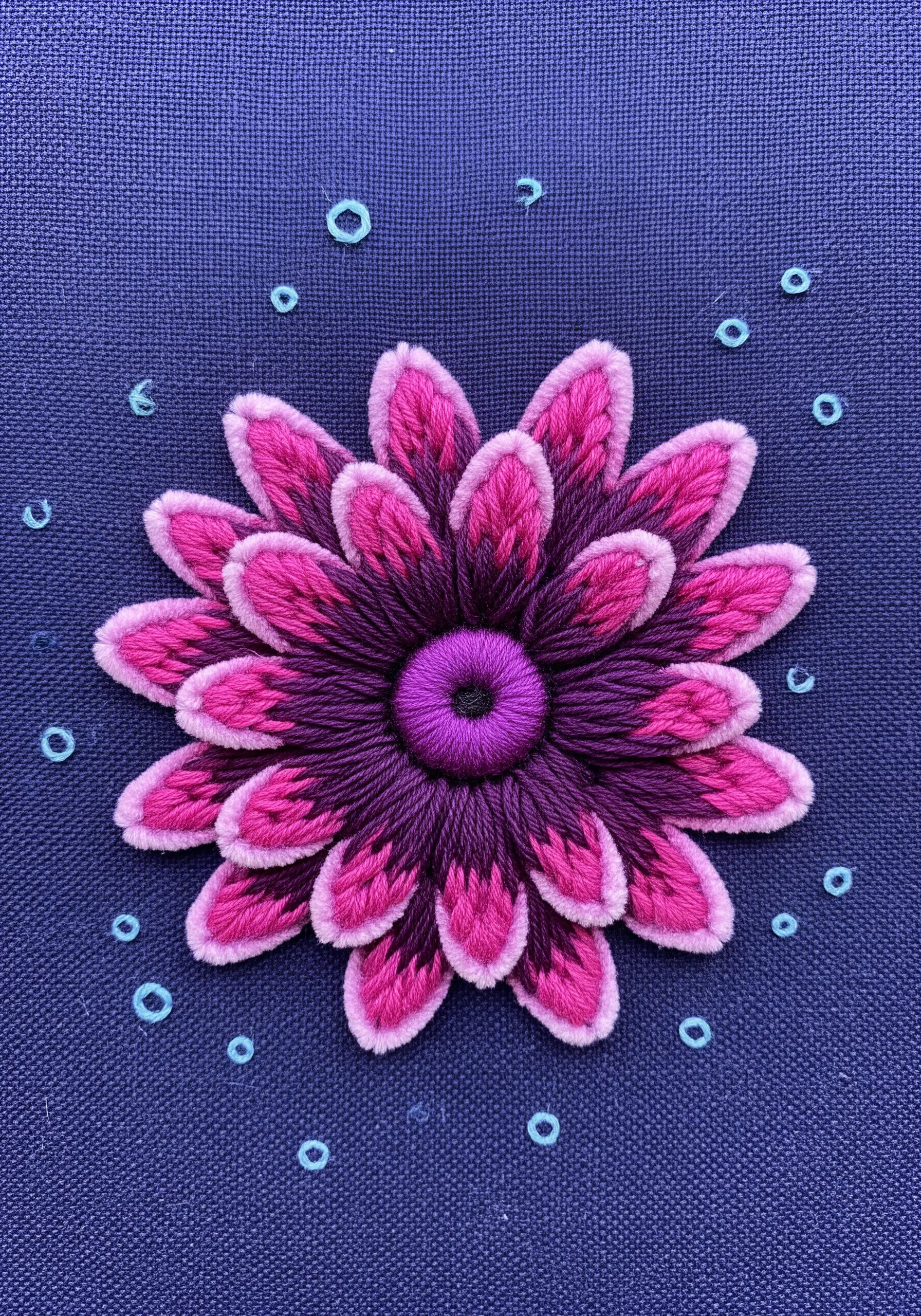 A dimensional sea anemone flower embroidered with pink and purple turkey work on dark blue fabric.