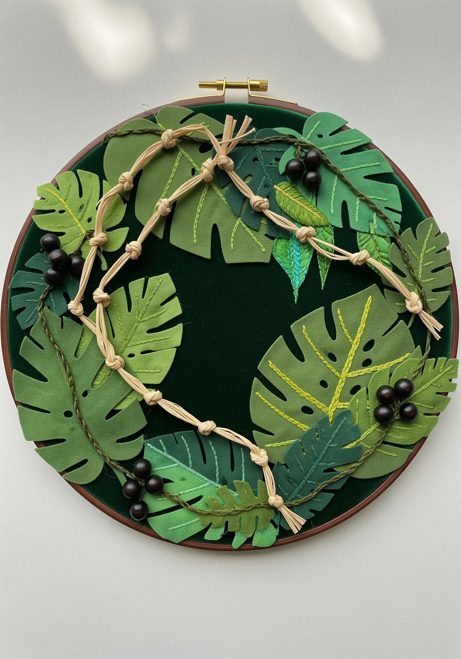 A 3D wreath in a hoop made from green felt leaves, macrame cord, and black beads.