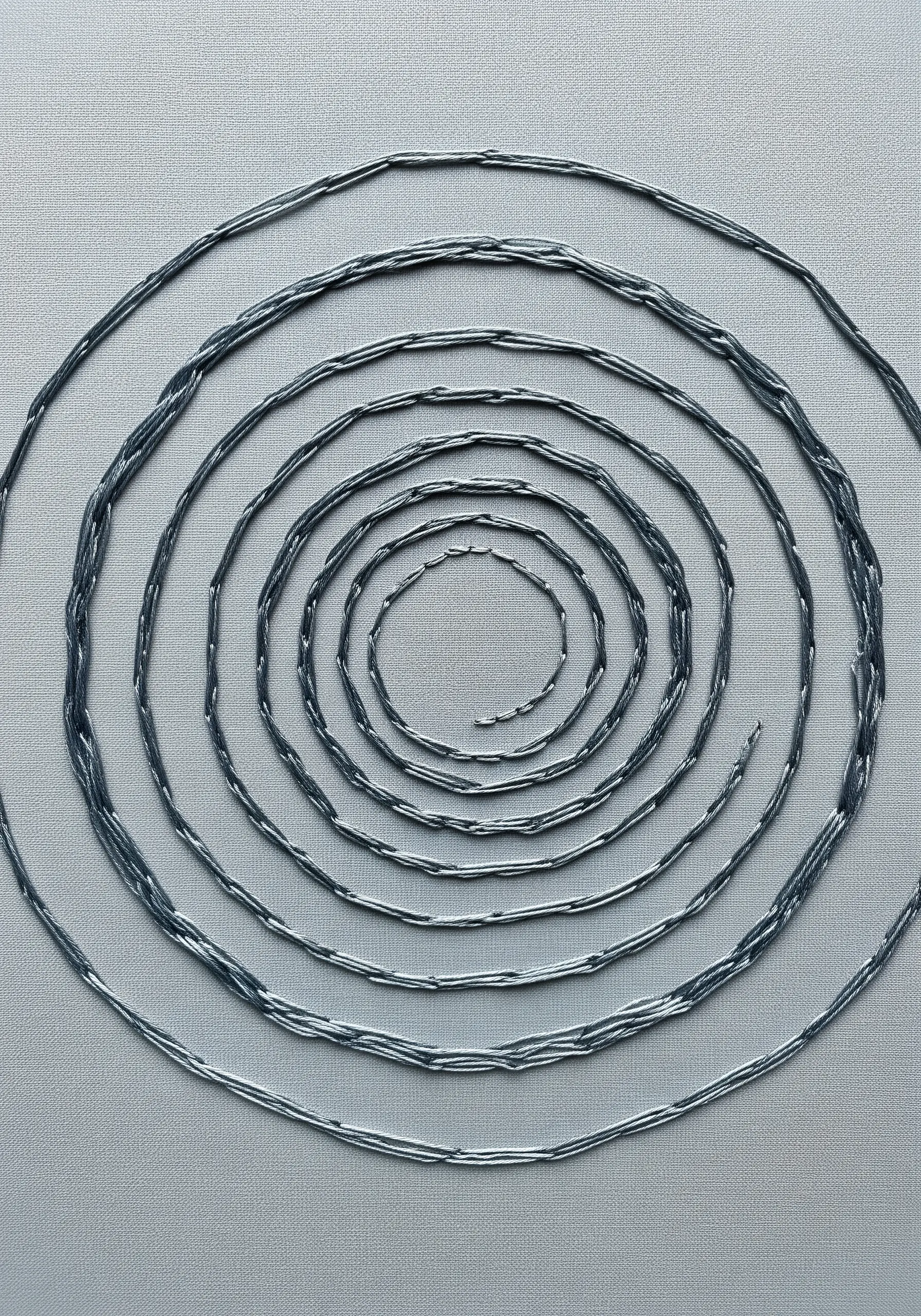 A close-up of an embroidered spiral made with a textured, wrapped stitch in grey thread.