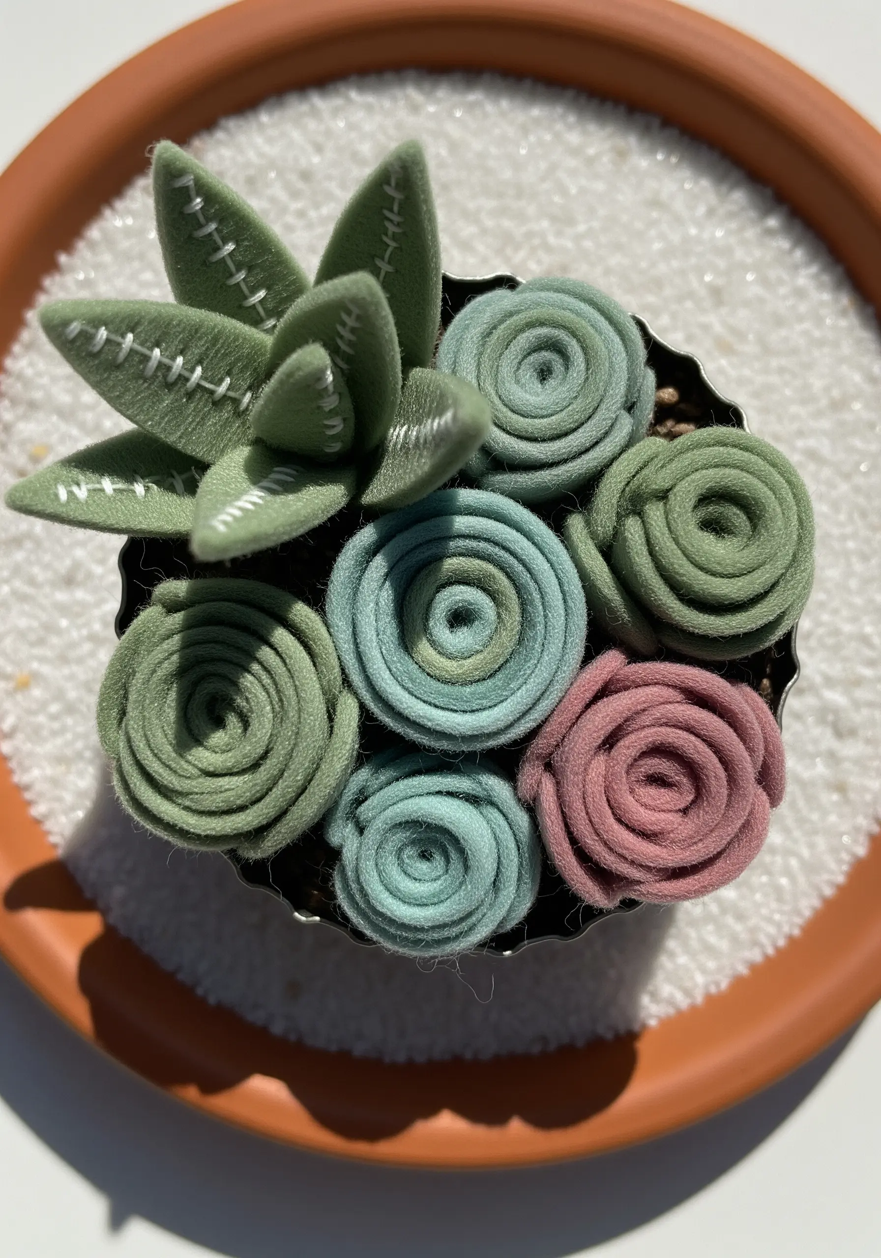 A small pot filled with felt succulents made from rolled and stitched green and pink felt.