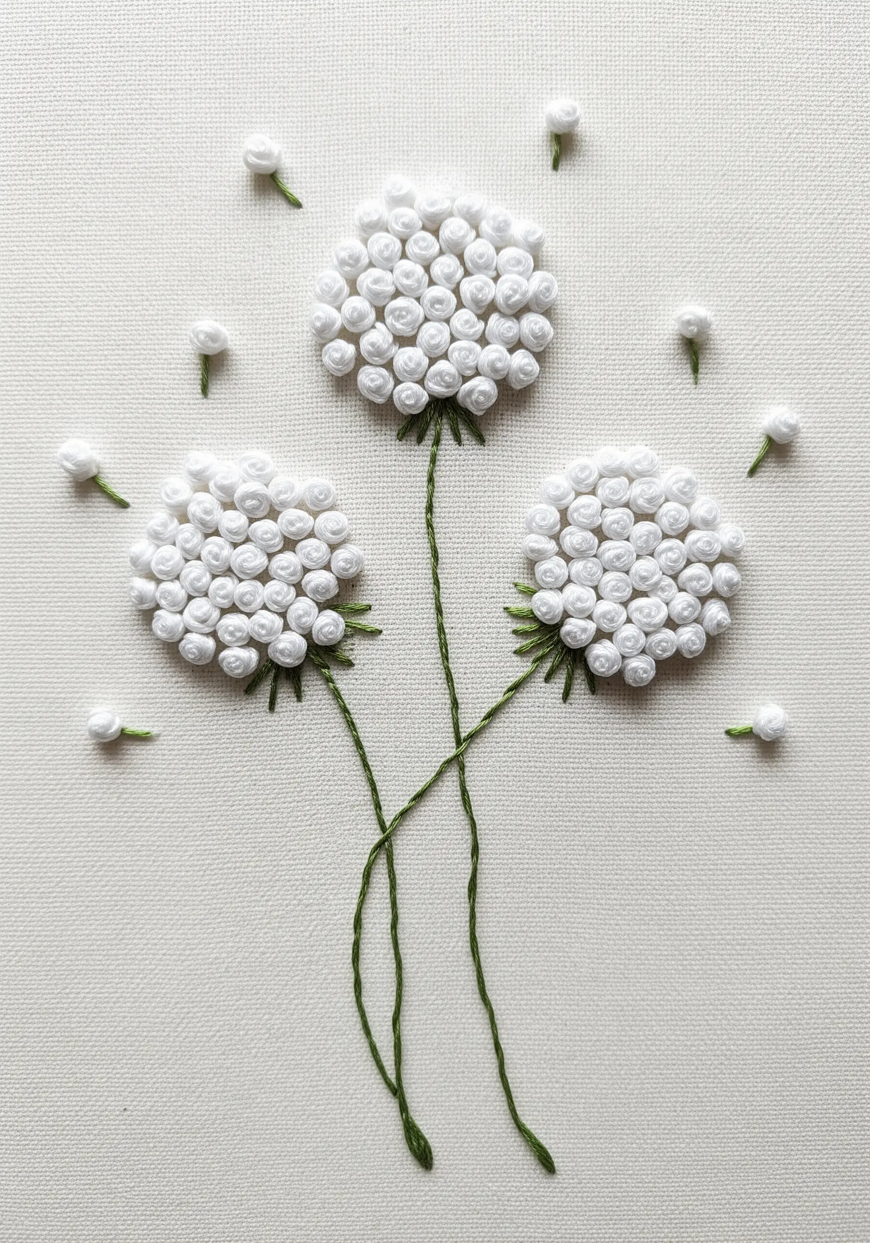 Three-dimensional dandelions made from white bullion knots with delicate green stems.