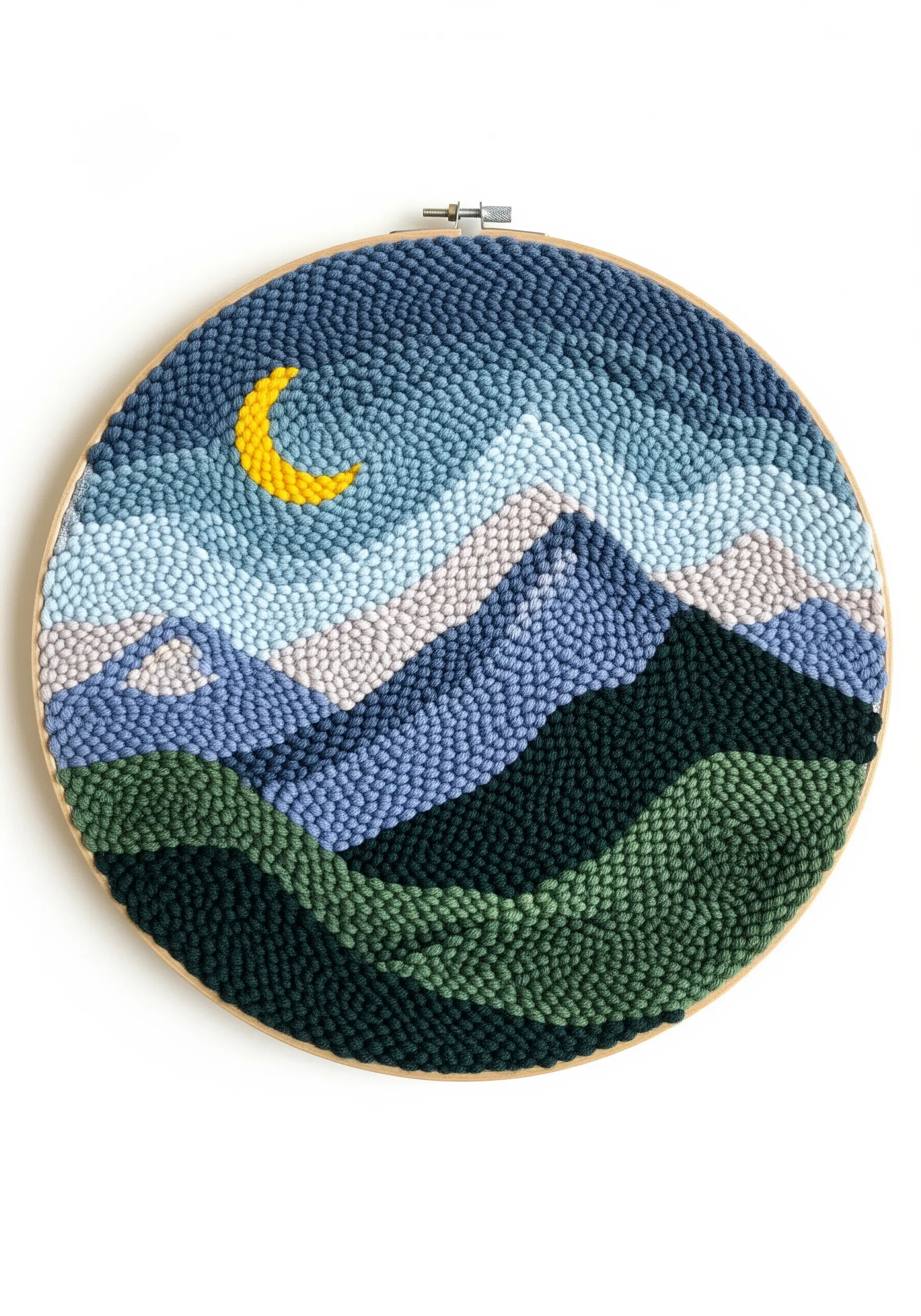 A punch needle hoop depicting rolling mountains in shades of blue and green with a yellow moon.