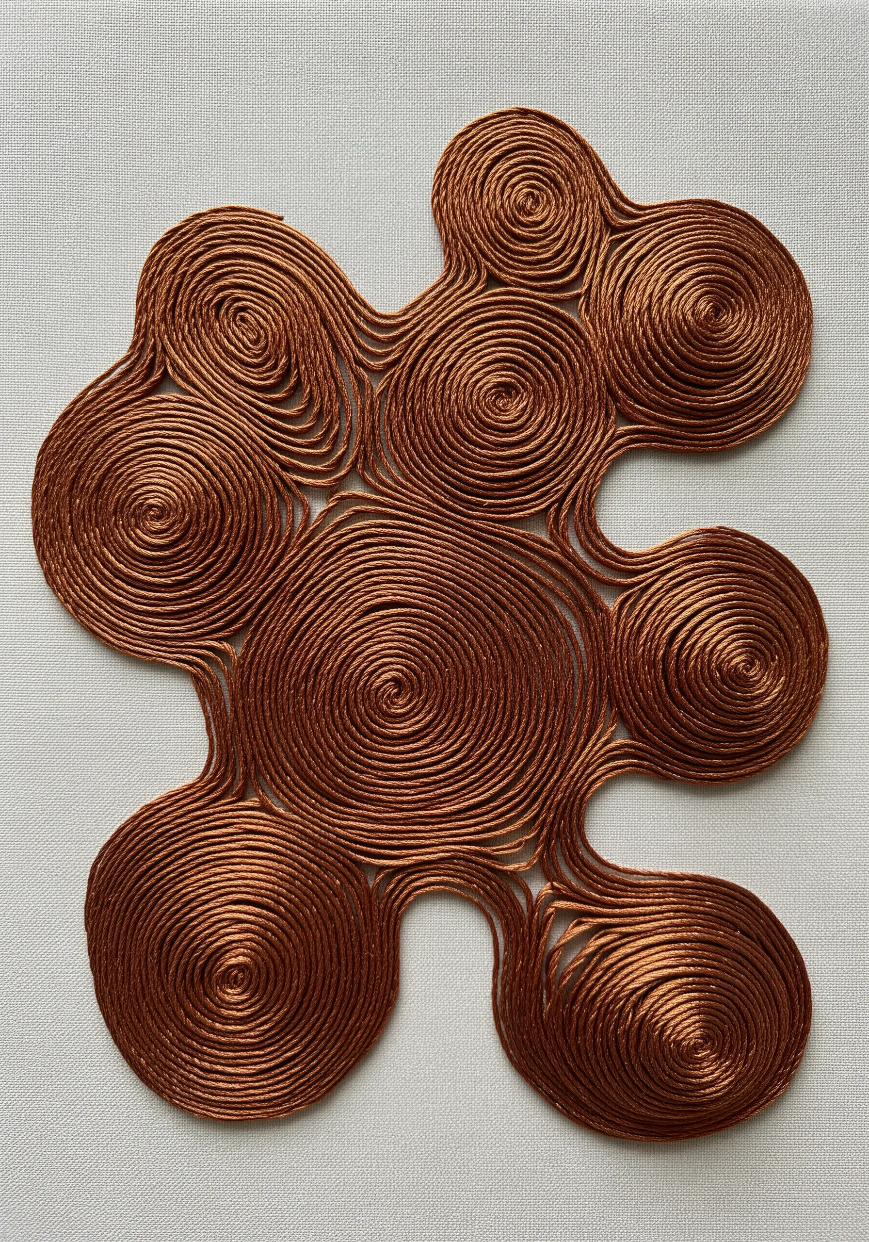 A sculptural piece made of coiled copper metallic cord on a neutral fabric background.