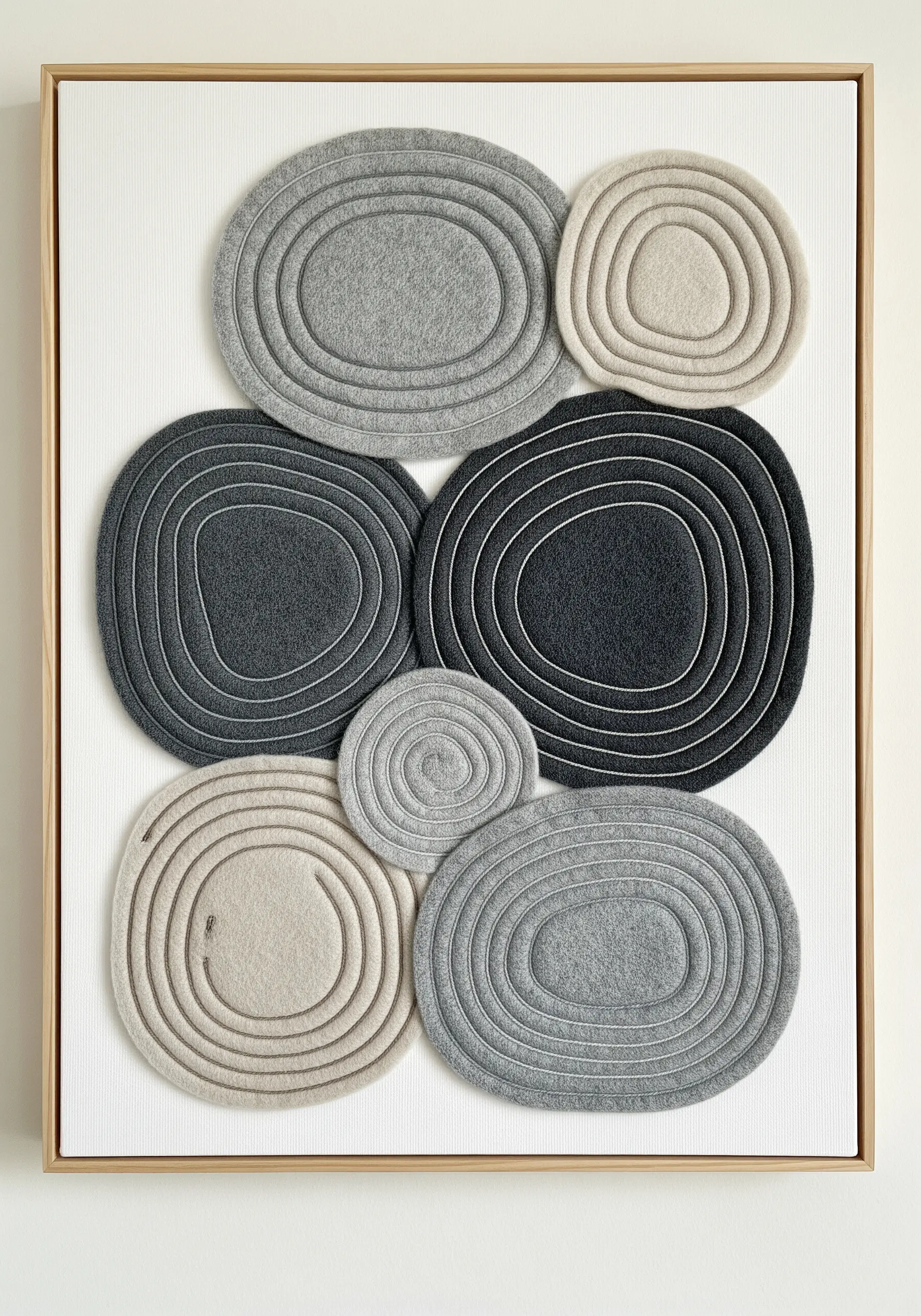 Minimalist wall art featuring layered gray and cream felt shapes with concentric stitching.