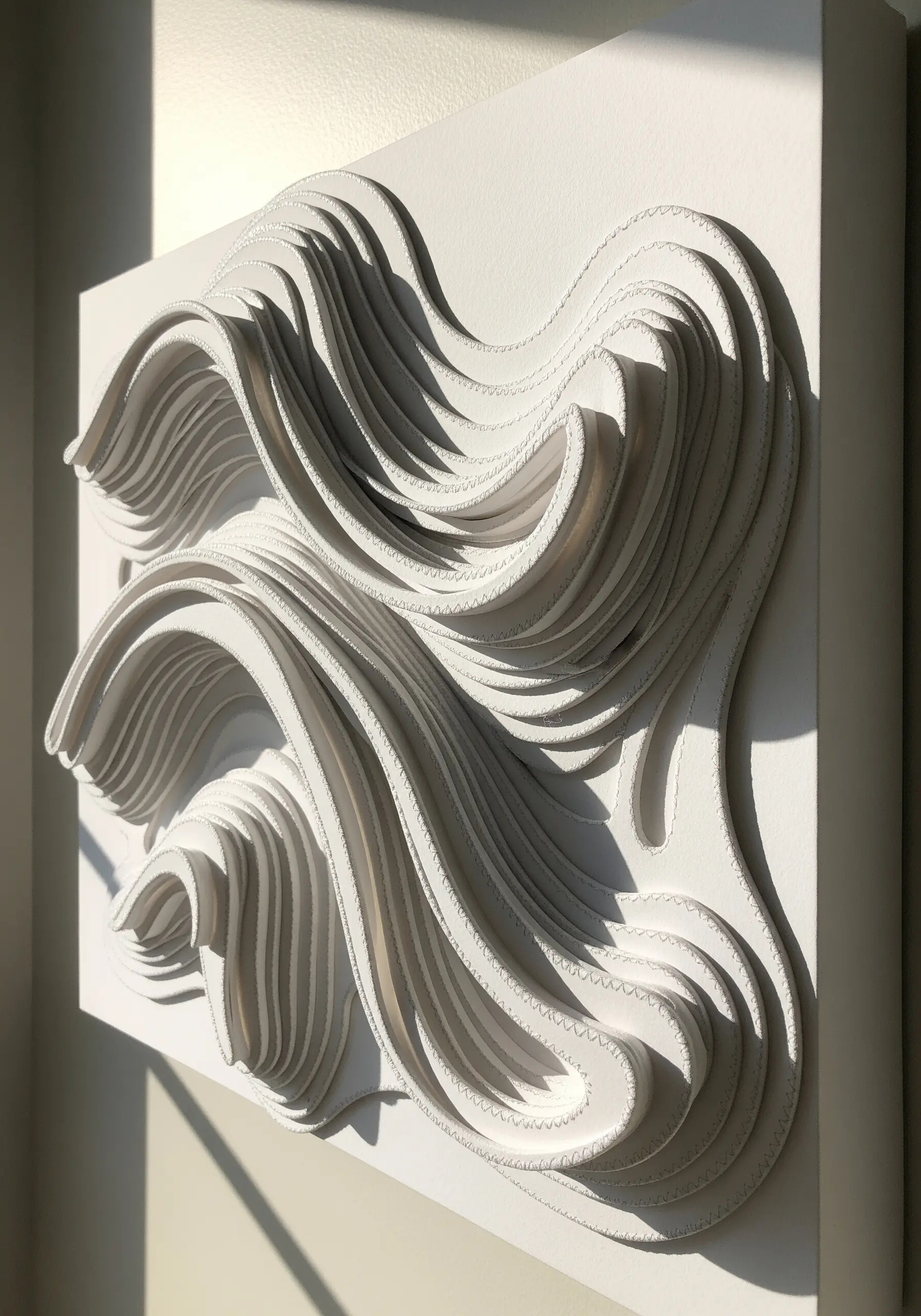 A white wall sculpture made from layers of cut paper with stitched edges, creating a wavy form.