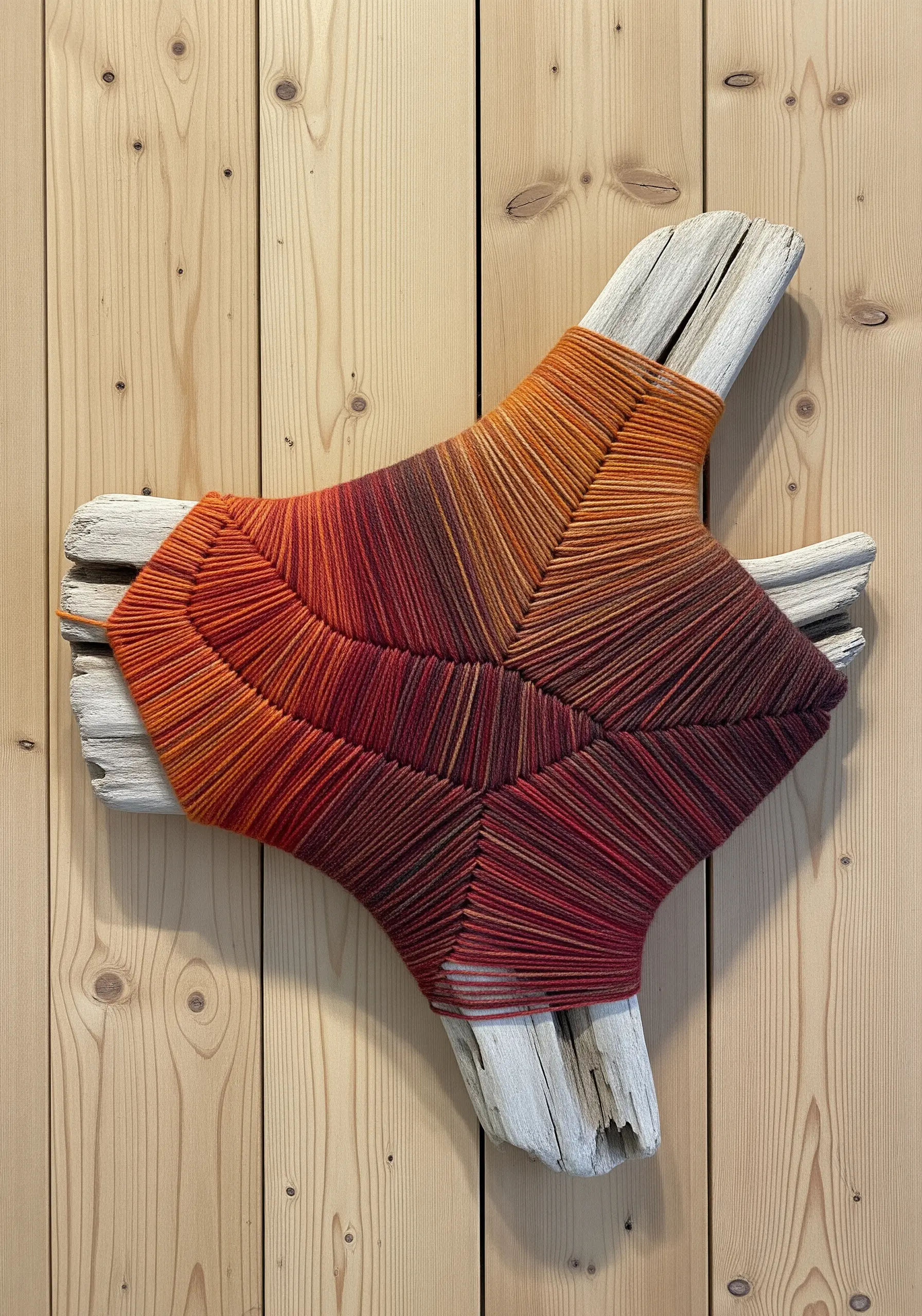 Driftwood pieces wrapped tightly in a gradient of orange, red, and brown yarn.
