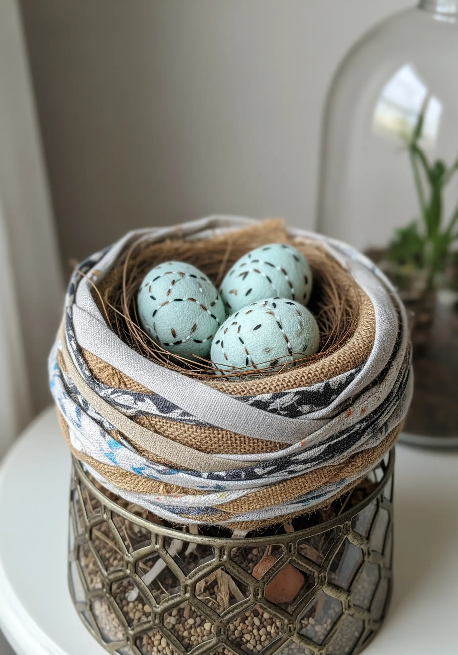 A bird's nest sculpture crafted from coiled strips of burlap and patterned fabric.