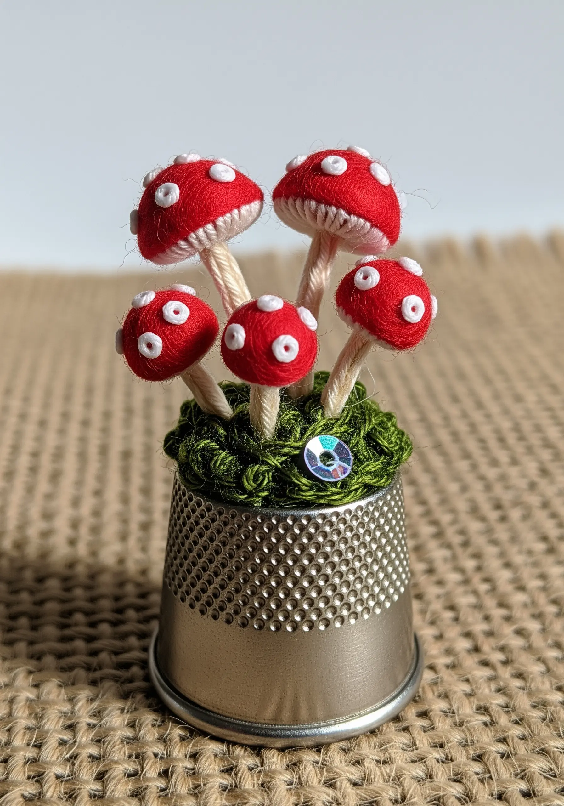 Tiny embroidered red and white mushrooms standing in a silver thimble.