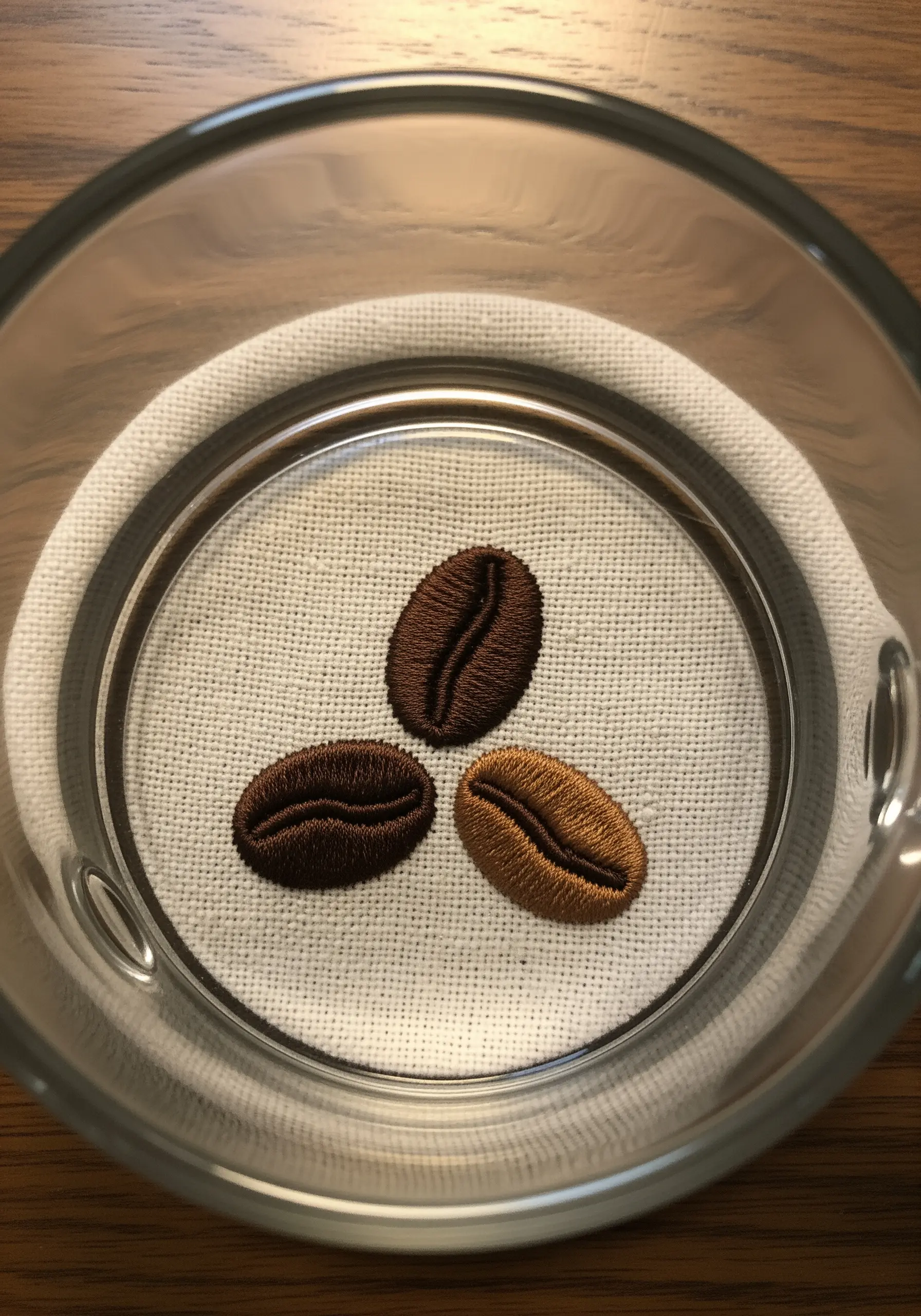 Three embroidered coffee beans with detailed satin stitch on light fabric.