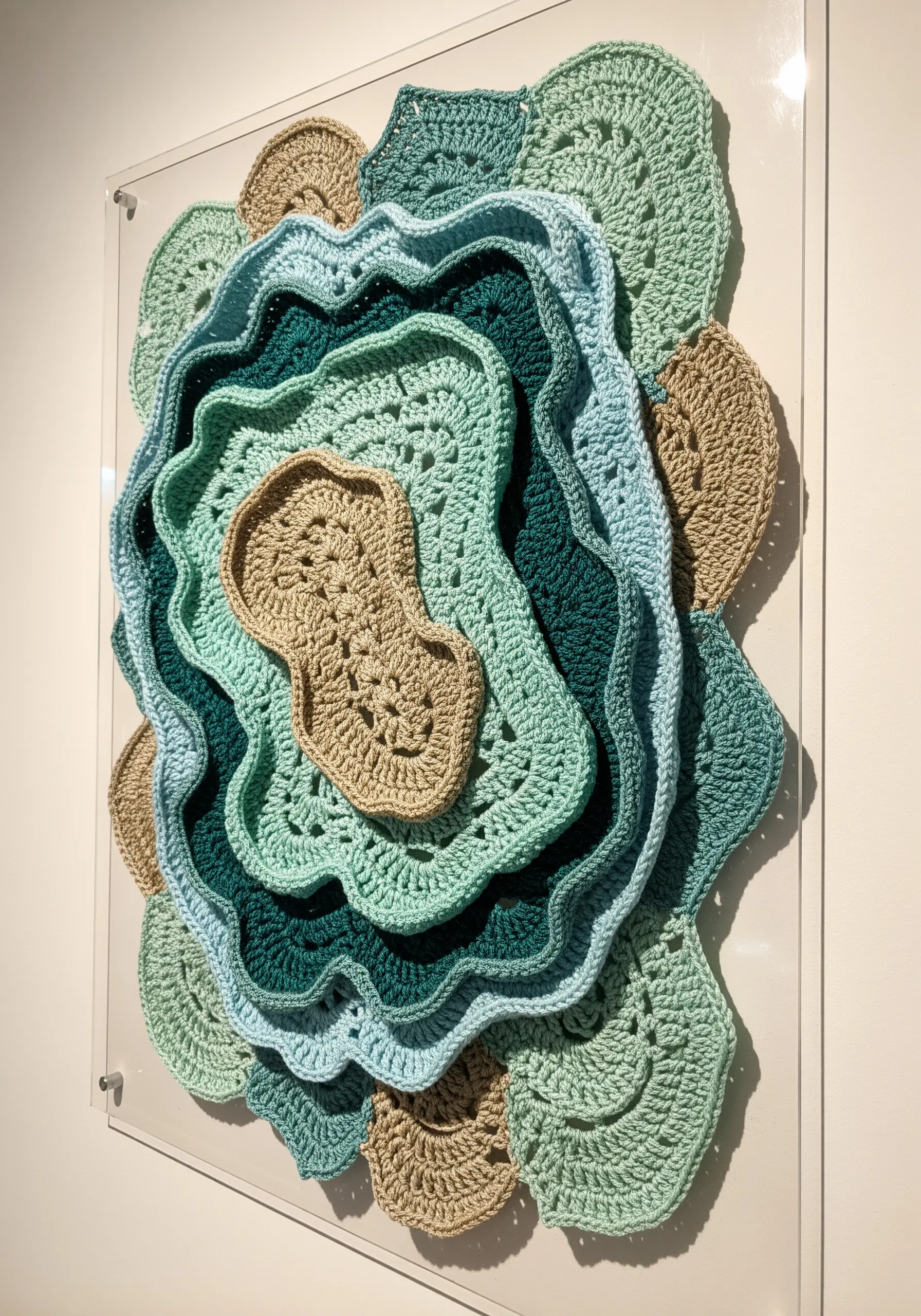 A 3D wall sculpture made of layered, freeform crochet pieces in shades of green and beige.