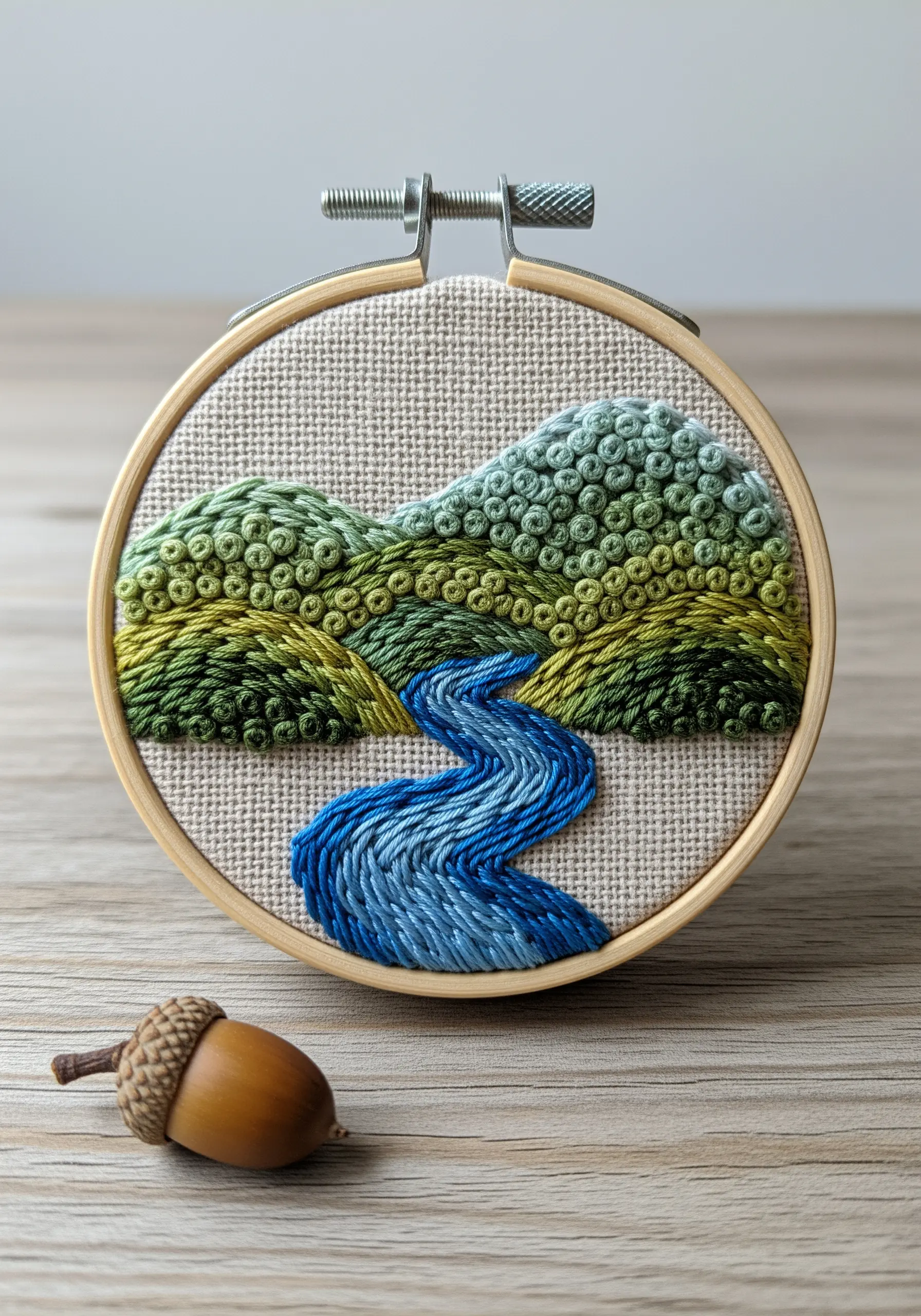 Embroidered landscape with French knot hills and a satin stitch river in a small hoop.