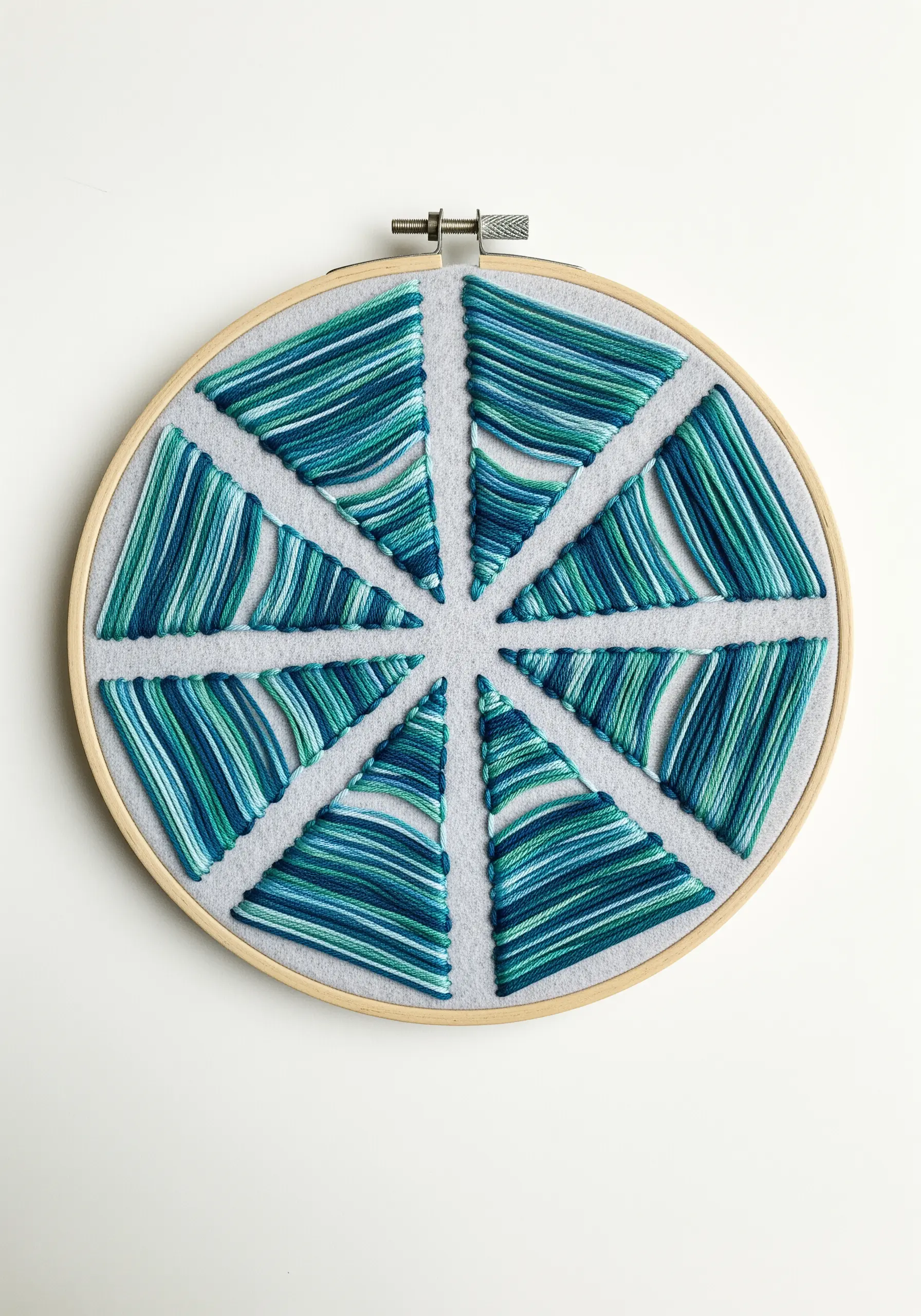 Hoop art with a segmented circle filled with satin stitches using blue and green variegated thread.