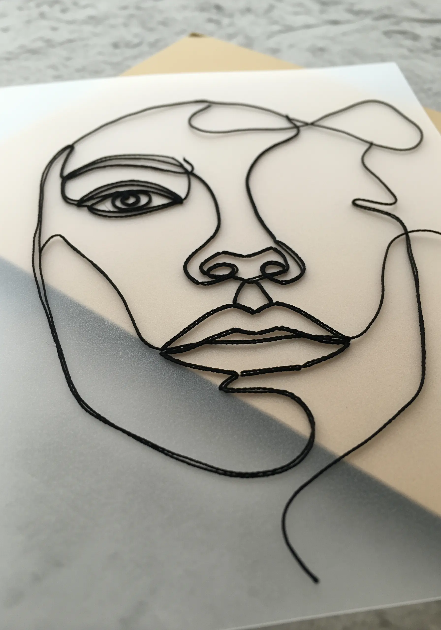 Continuous line face portrait embroidered with black thread on translucent vellum paper
