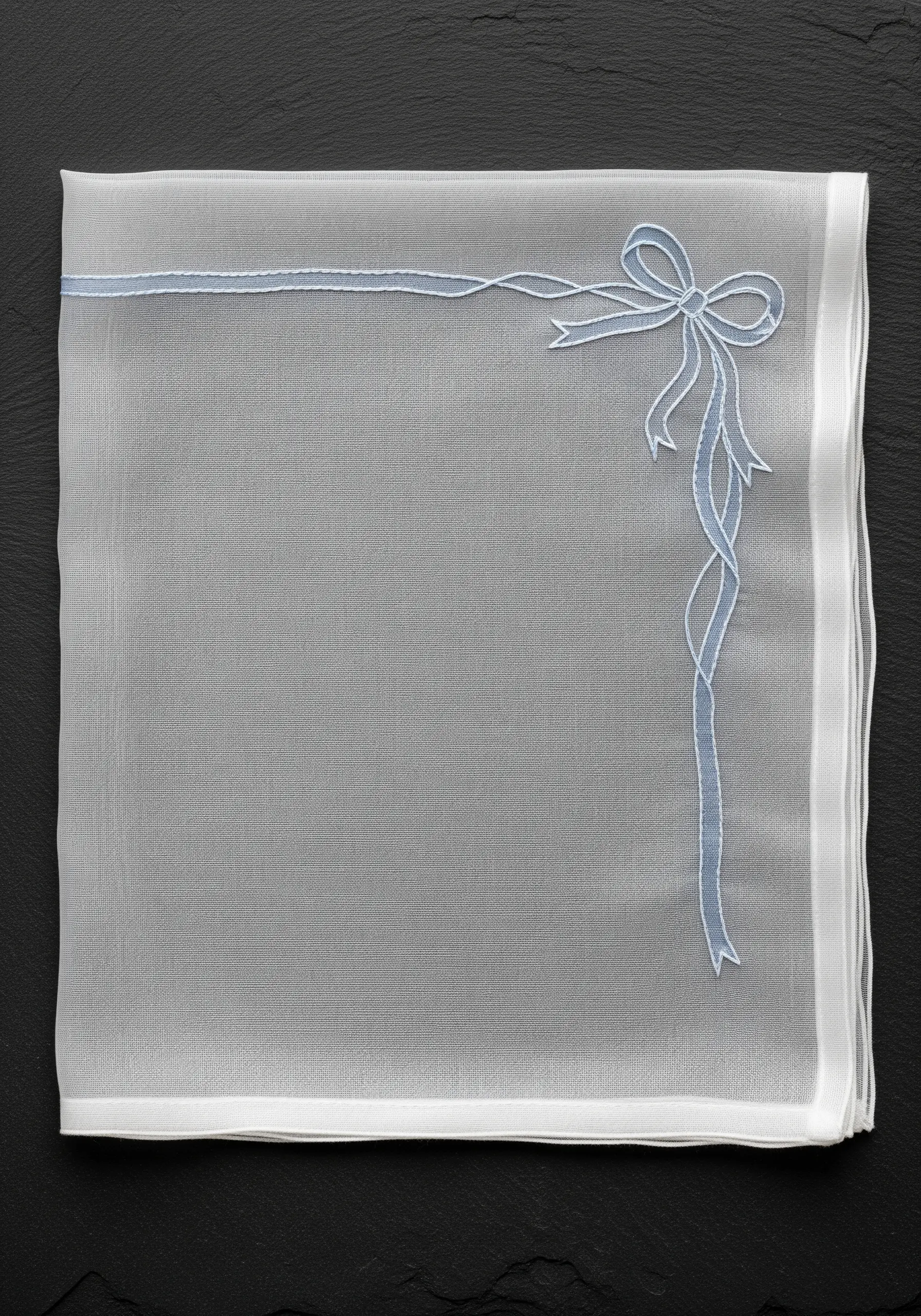 A delicate blue ribbon and bow embroidered on a sheer white napkin using shadow work.