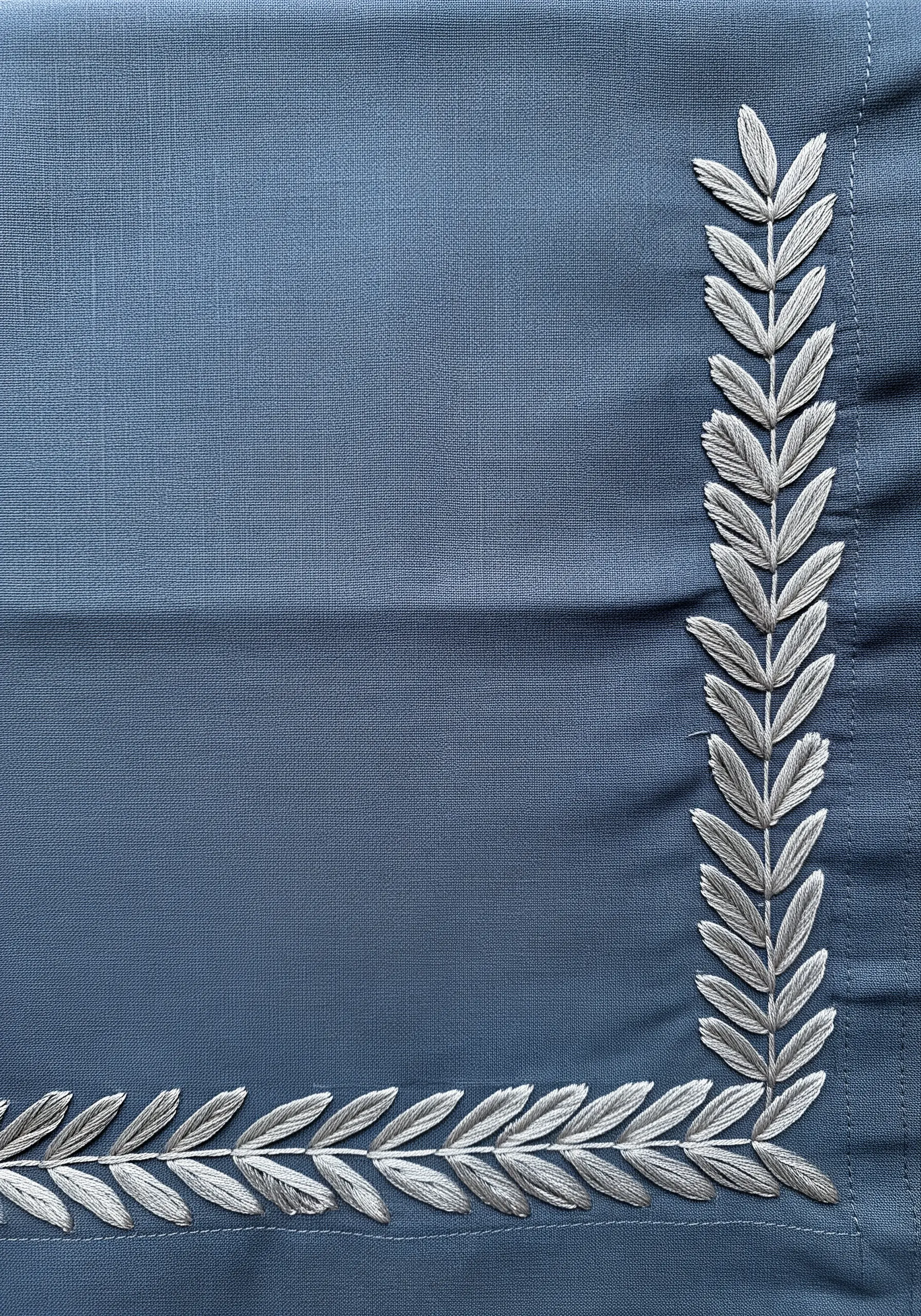 Silver-gray laurel leaf border stitched on a dusty blue-gray napkin.