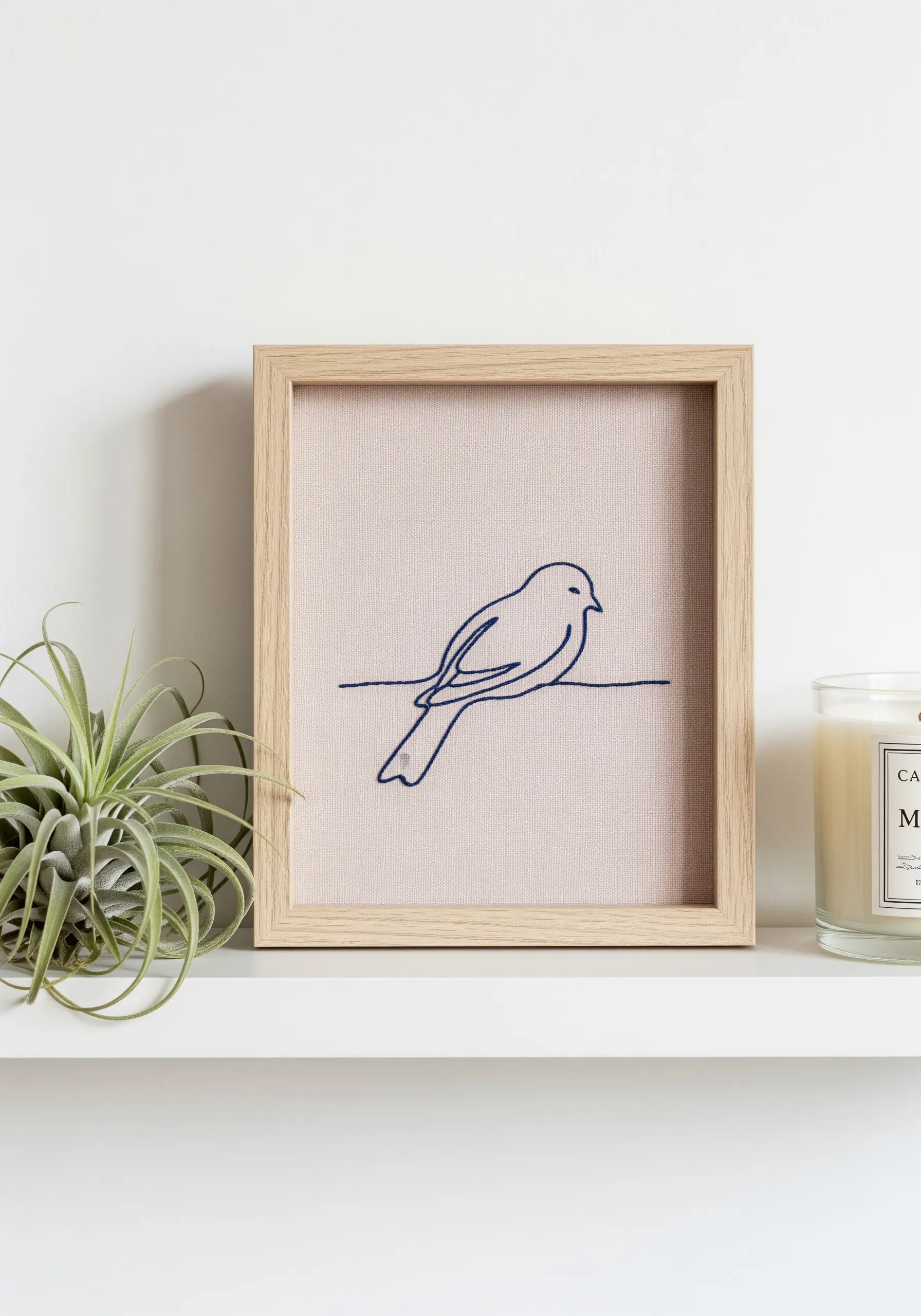 Minimalist navy blue line-art bird embroidered on pale pink fabric in a wooden frame.