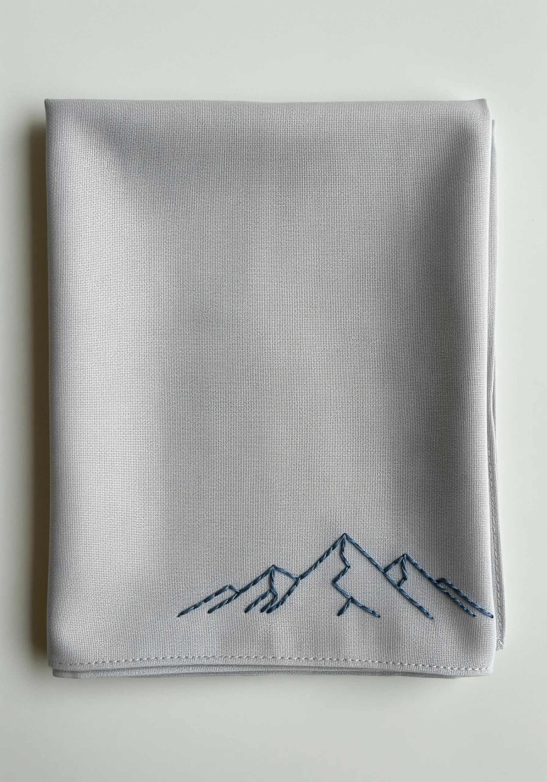 A minimalist mountain range outline stitched in dark thread on a light grey handkerchief.
