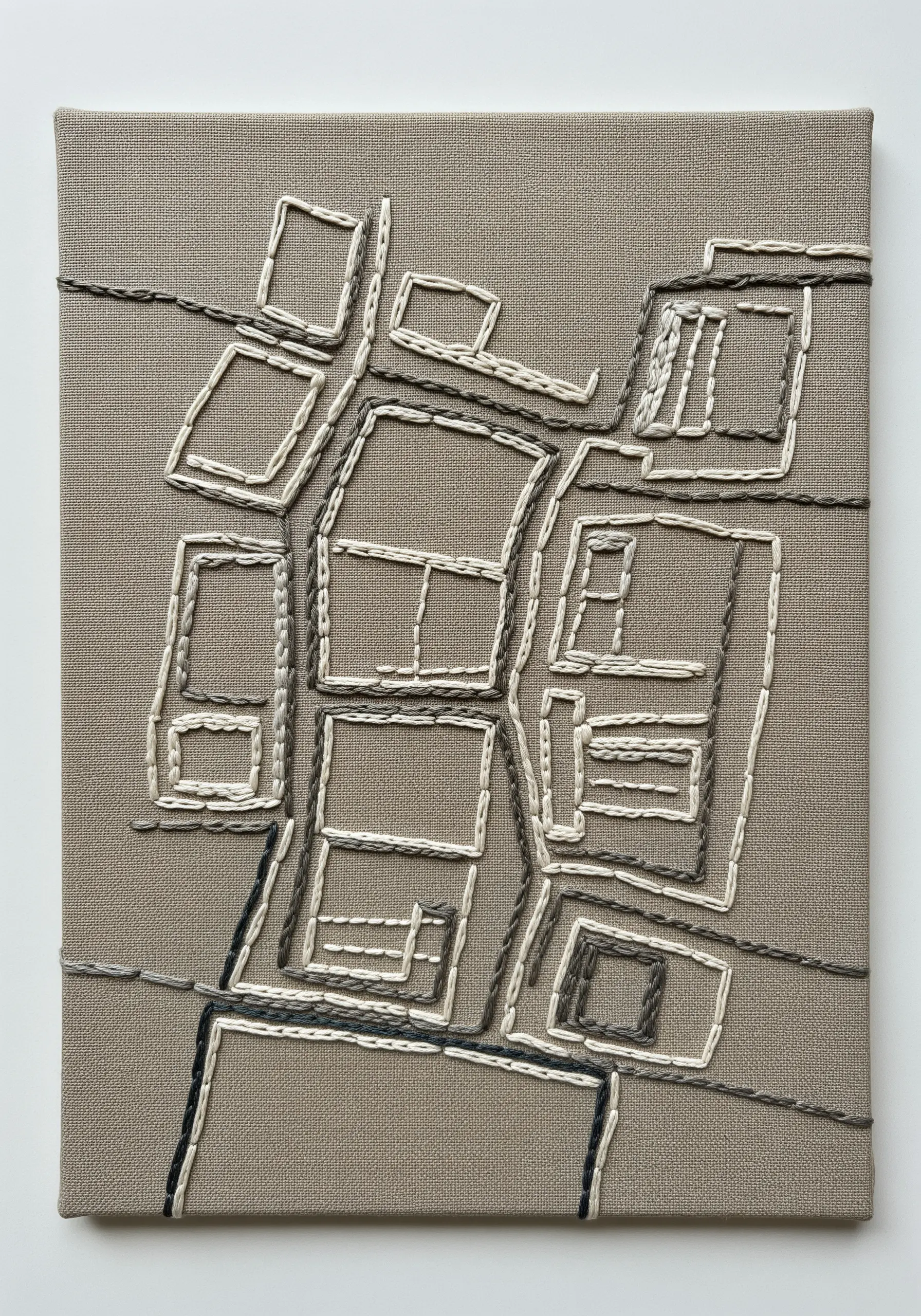 An abstract neighborhood map stitched in neutral grays and creams on taupe canvas.