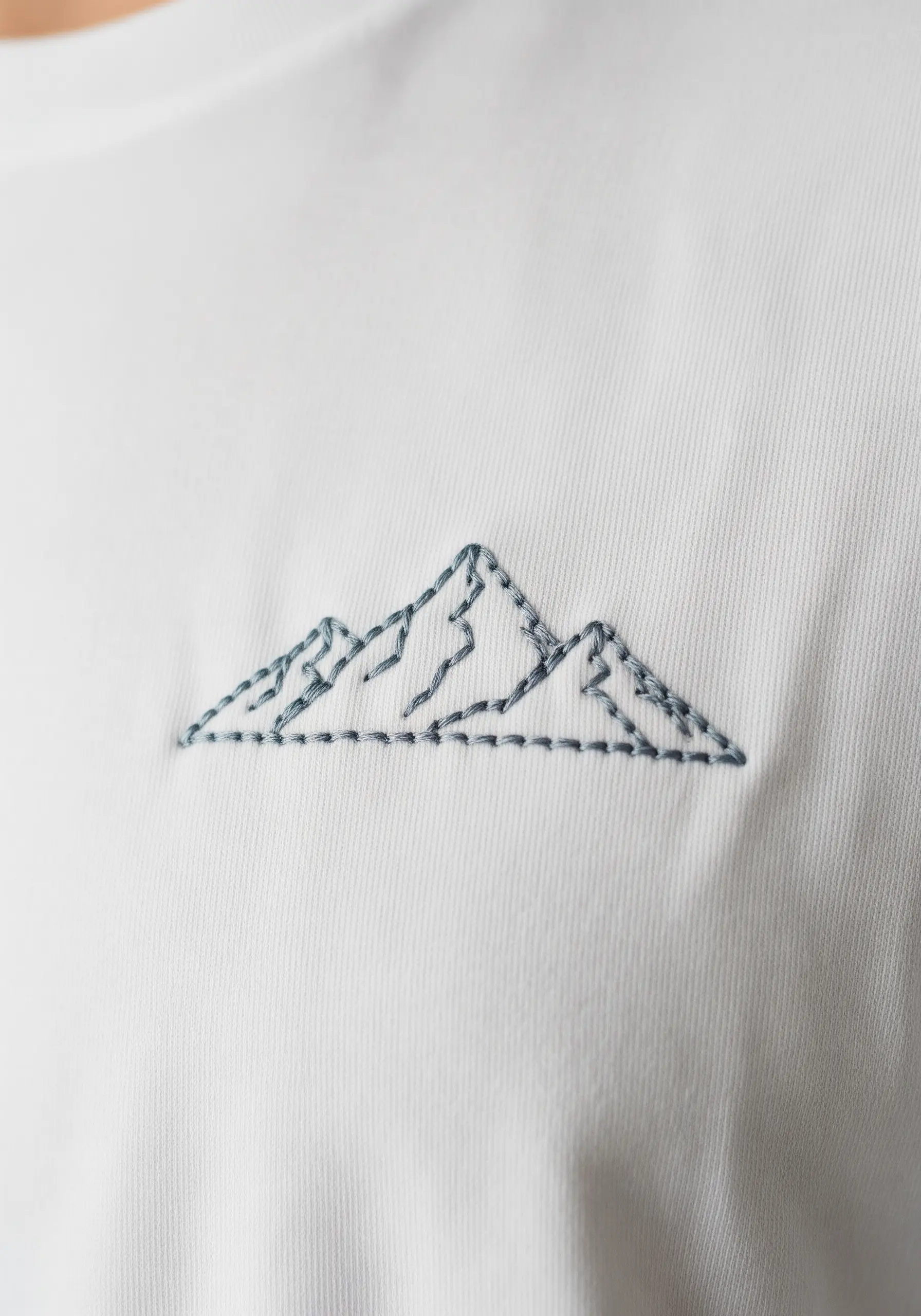 A minimal mountain range outlined in grey thread on a white shirt.