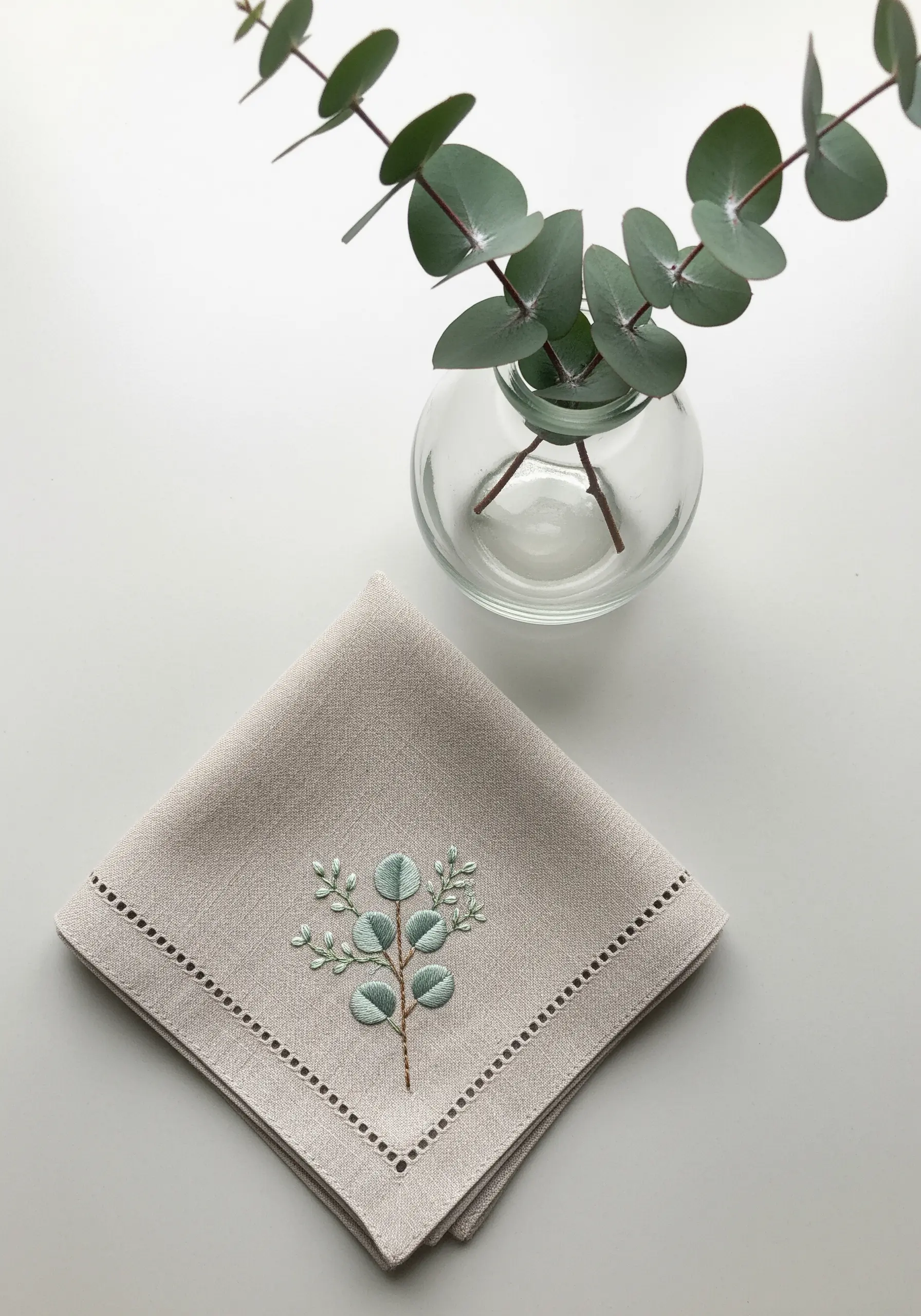 A delicate eucalyptus branch with green and blue leaves on a beige handkerchief.