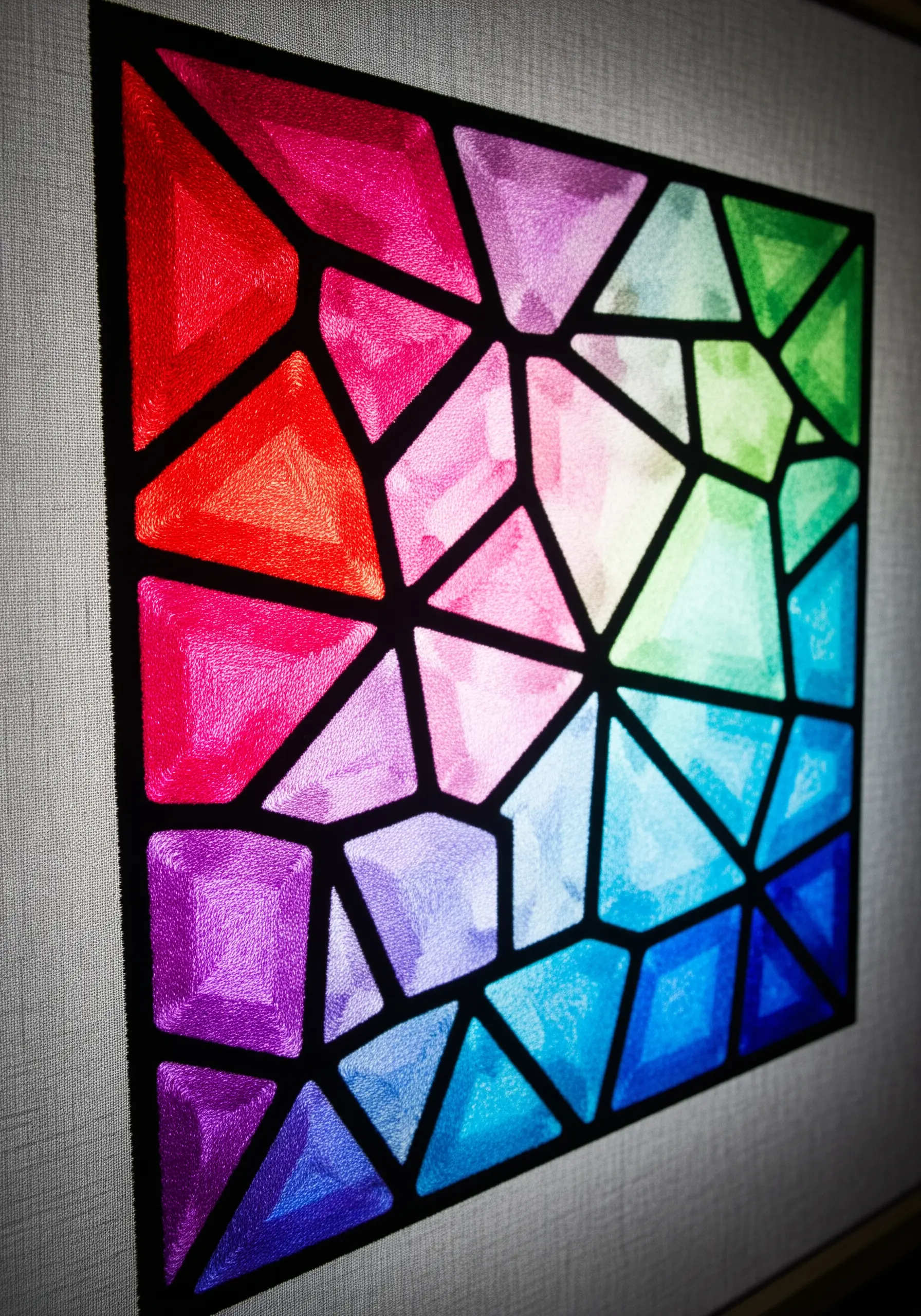 A geometric stained-glass pattern filled with satin stitch in a full-spectrum gradient.