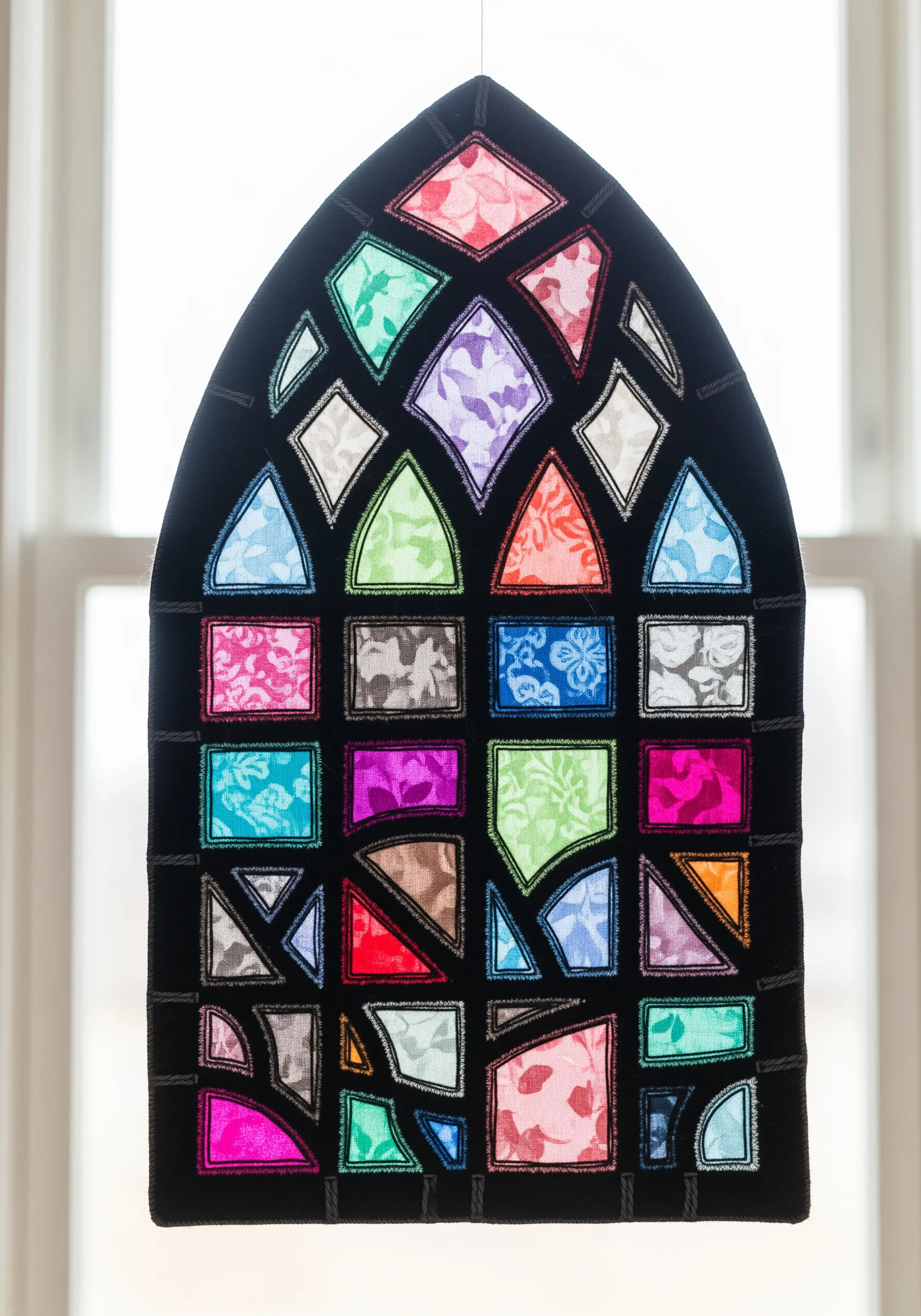 A textile art piece shaped like an arched window, with colorful fabric scraps resembling stained glass.