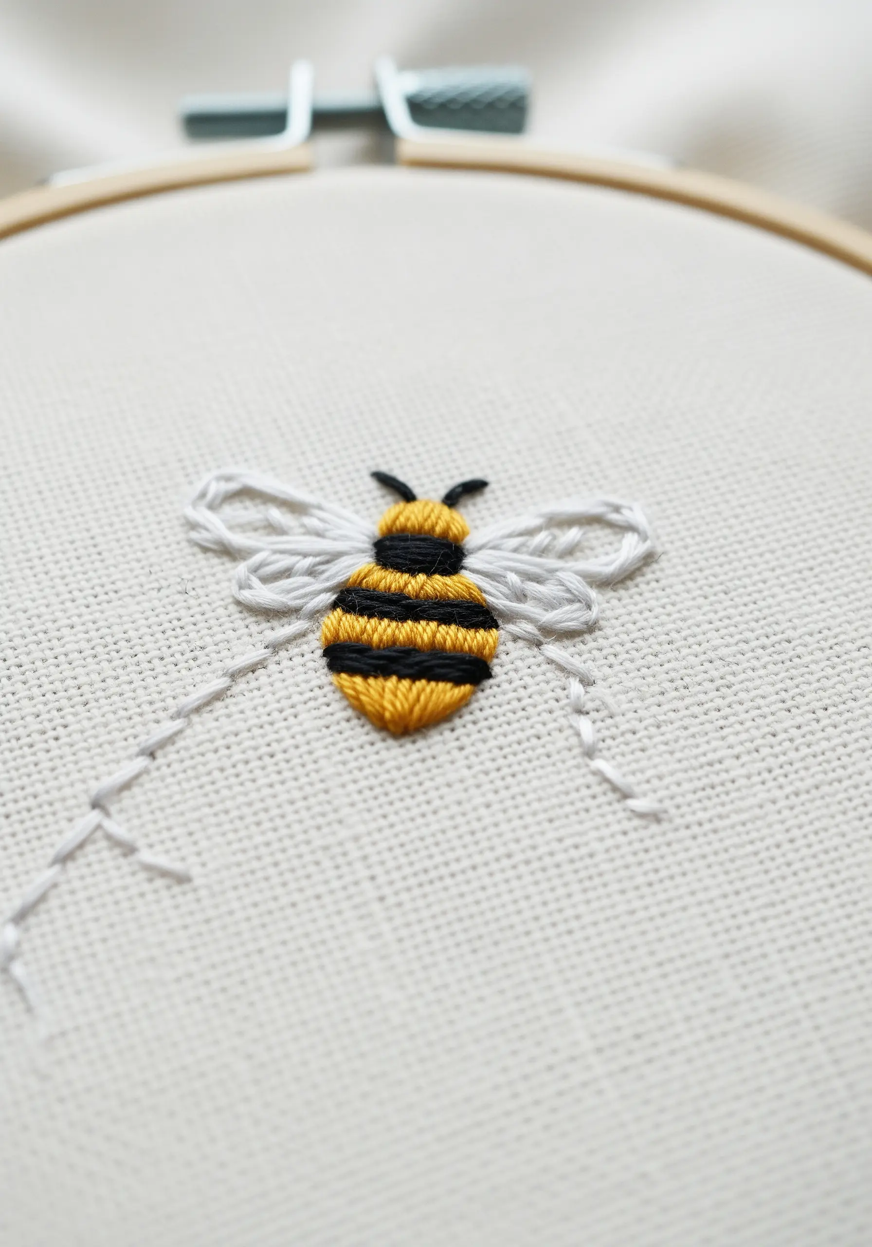 A close-up of a small embroidered bee with satin stitch stripes and delicate outline stitch wings.