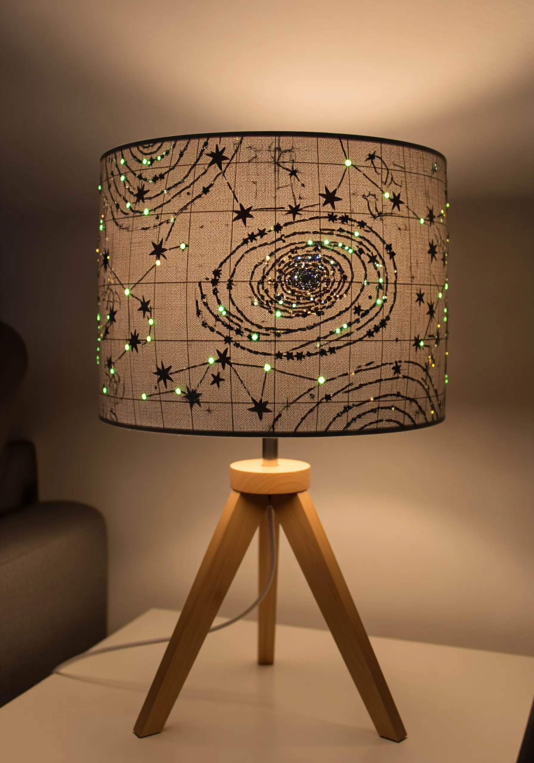 A drum lampshade embroidered with a galaxy pattern, illuminated from within by small lights.