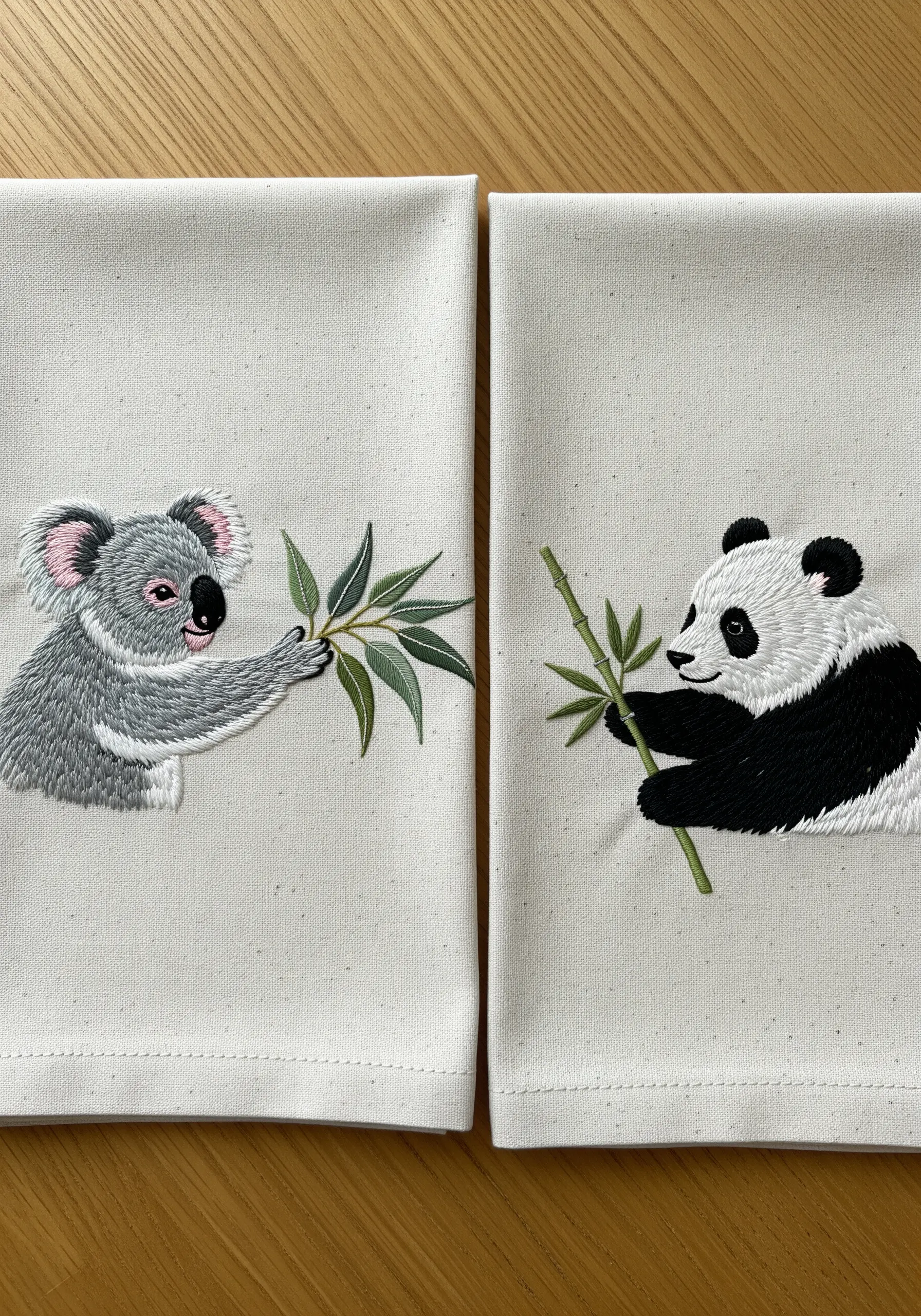 Two coordinating napkins, one with an embroidered koala and one with a panda, sharing a branch.