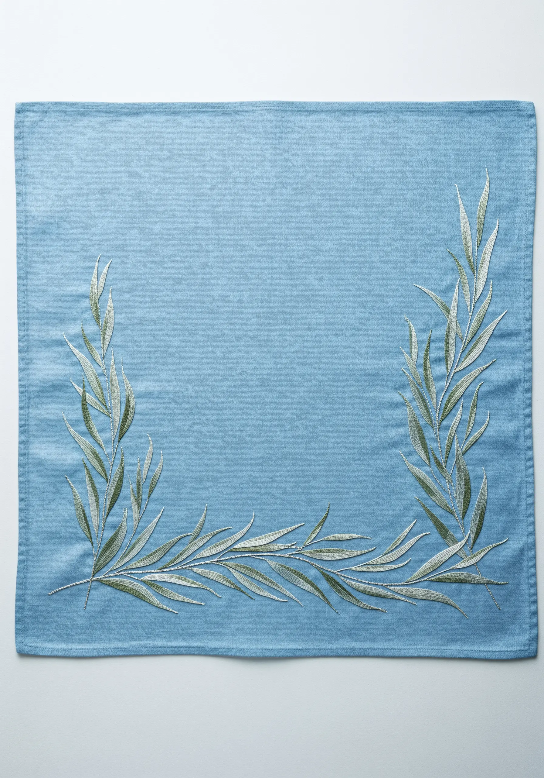 An L-shaped border of slender, silvery-green willow leaves on a dusty blue placemat.
