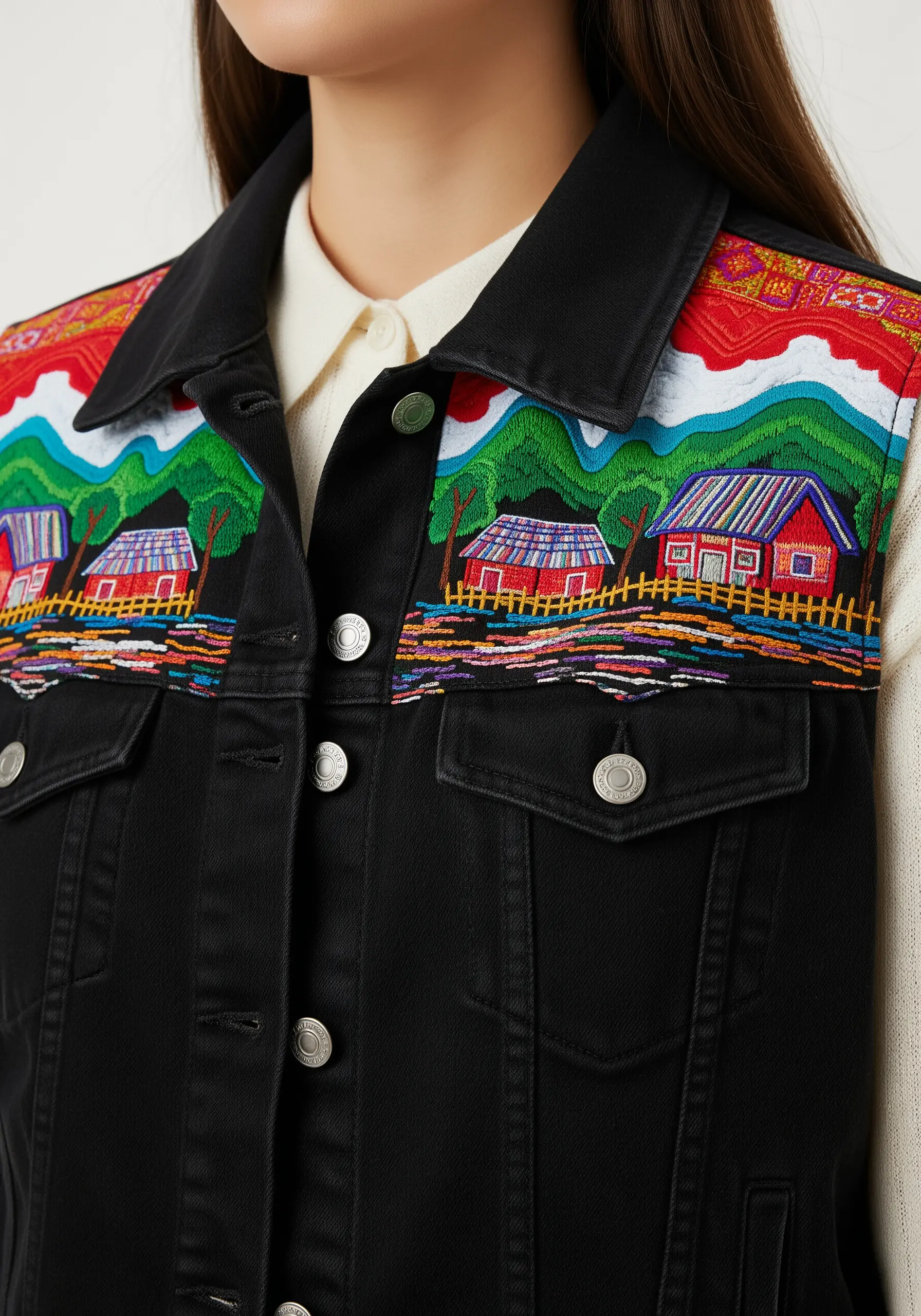 An embroidered landscape scene with houses and hills on the yoke of a black denim vest.