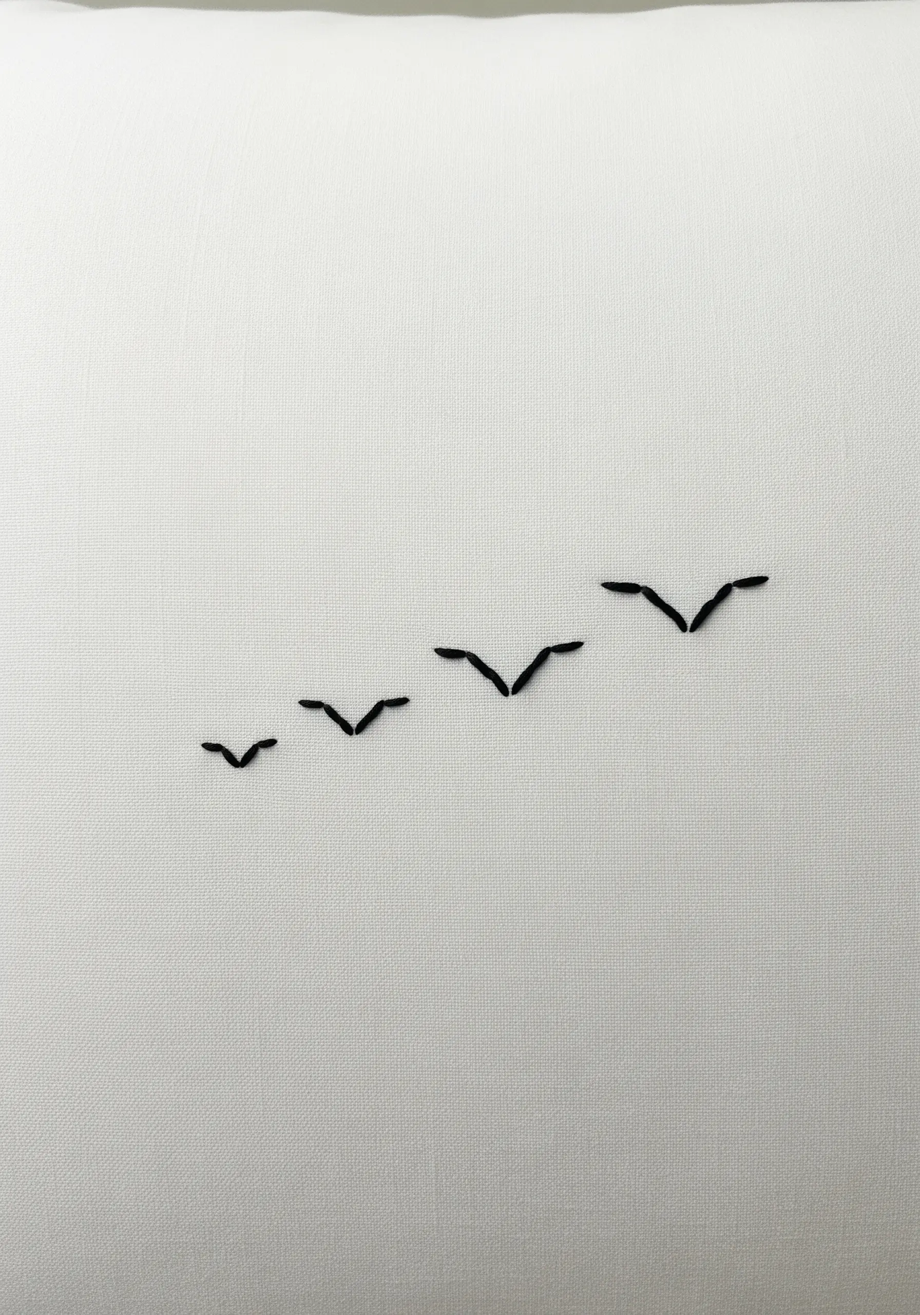 A minimalist flock of birds, made from simple 'V' stitches, flying across a white pillowcase.