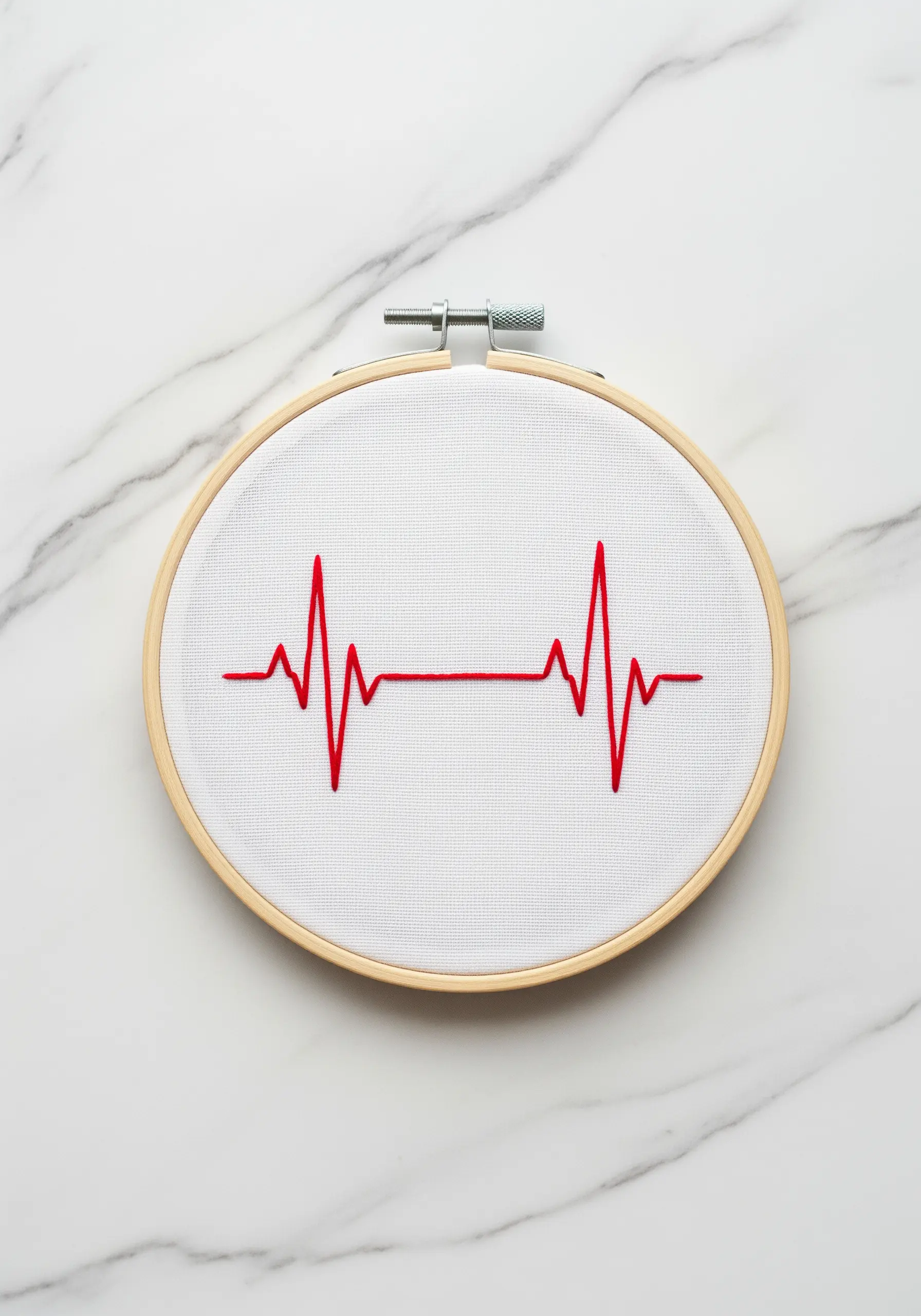 A simple red embroidered EKG heartbeat line on white fabric in a small hoop.
