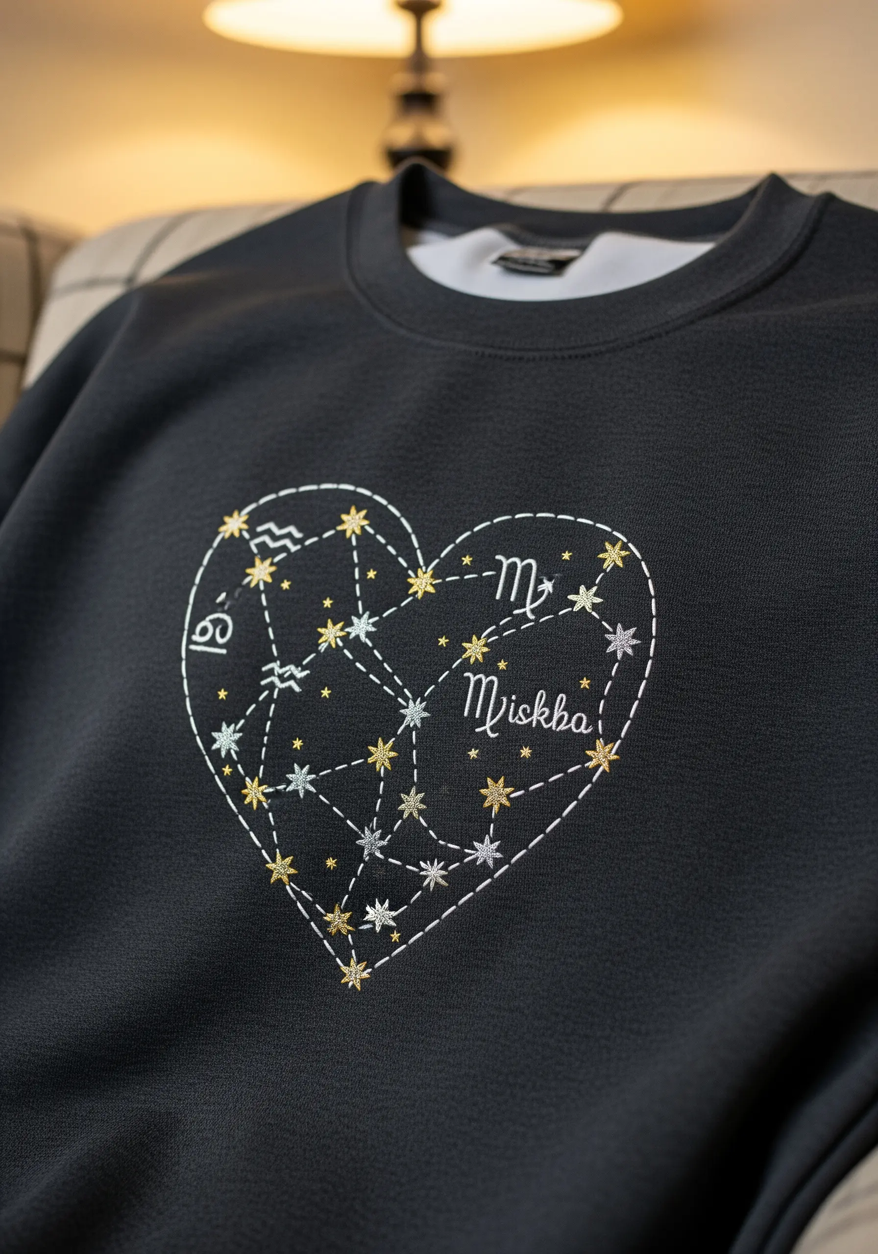 Embroidered heart-shaped constellation chart with zodiac signs on a black sweatshirt.