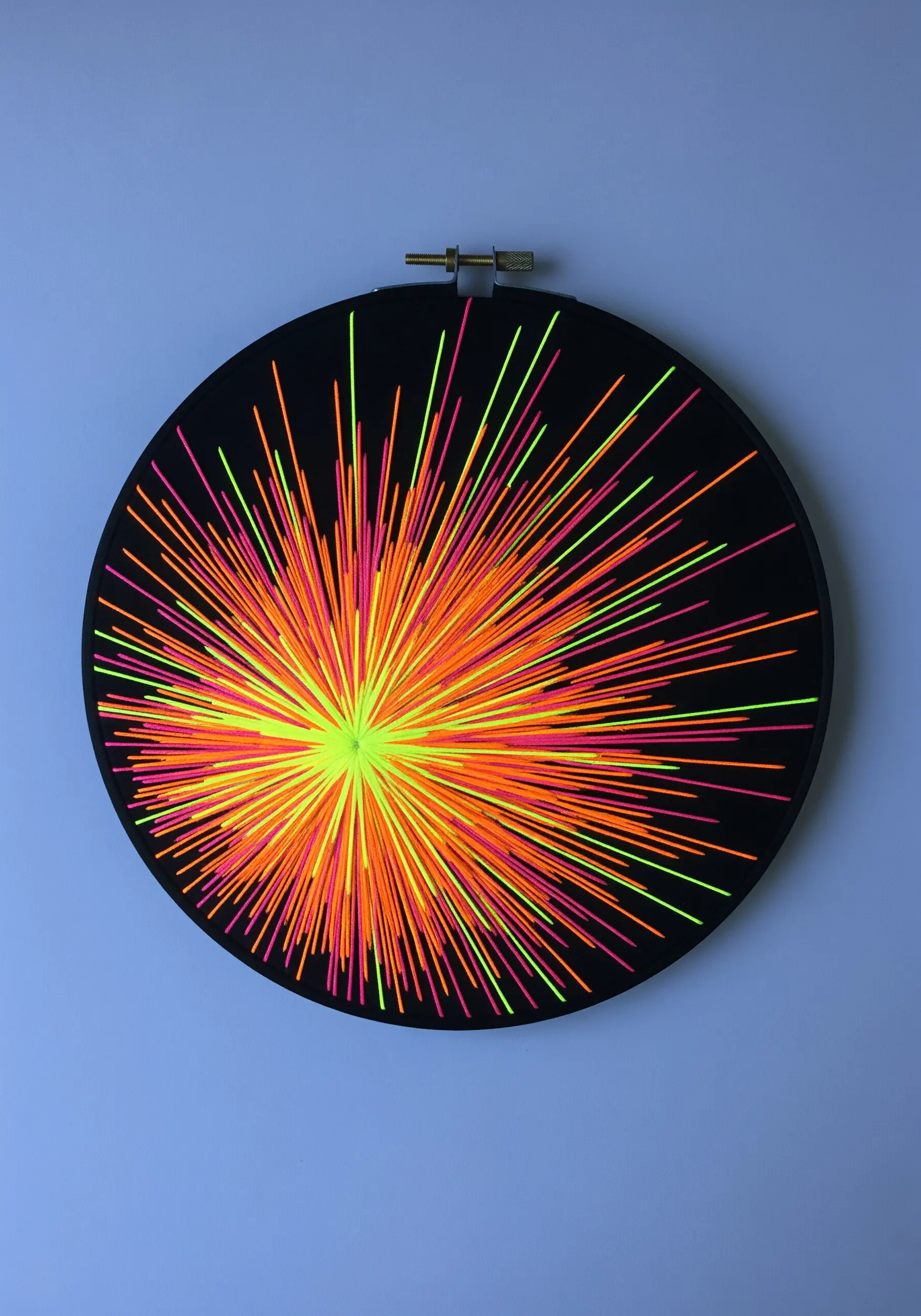 A vibrant starburst of radiating stitches in neon yellow, orange, and pink.
