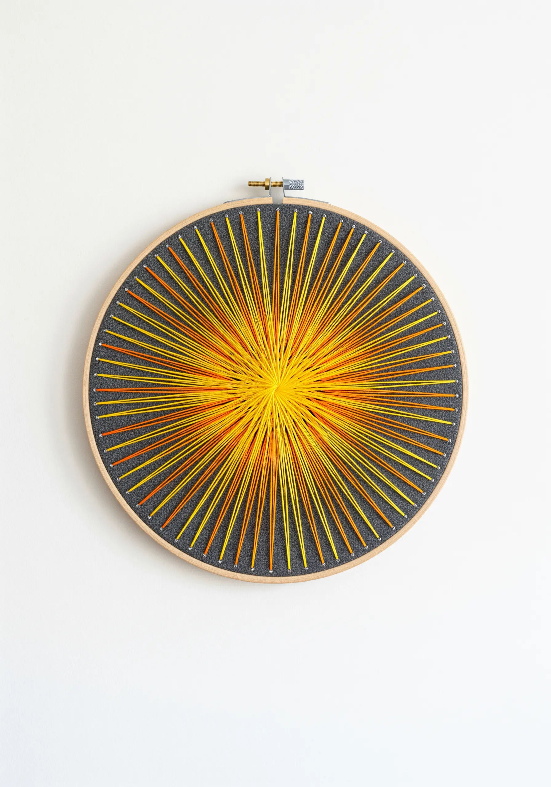 A radial sunburst design in a hoop, stitched with radiating lines of yellow and orange thread.