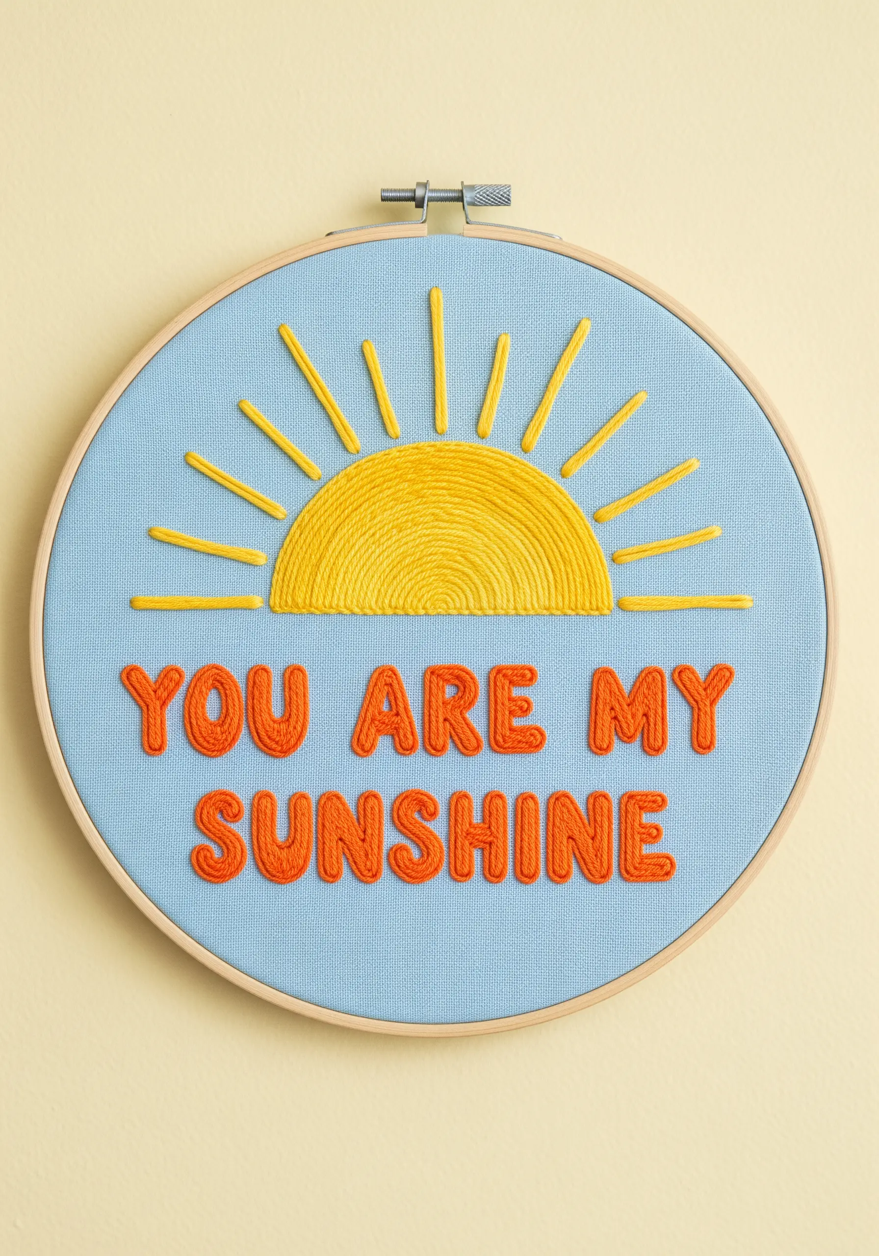 An embroidery hoop with 'You Are My Sunshine' in thick, textured yellow and orange thread.