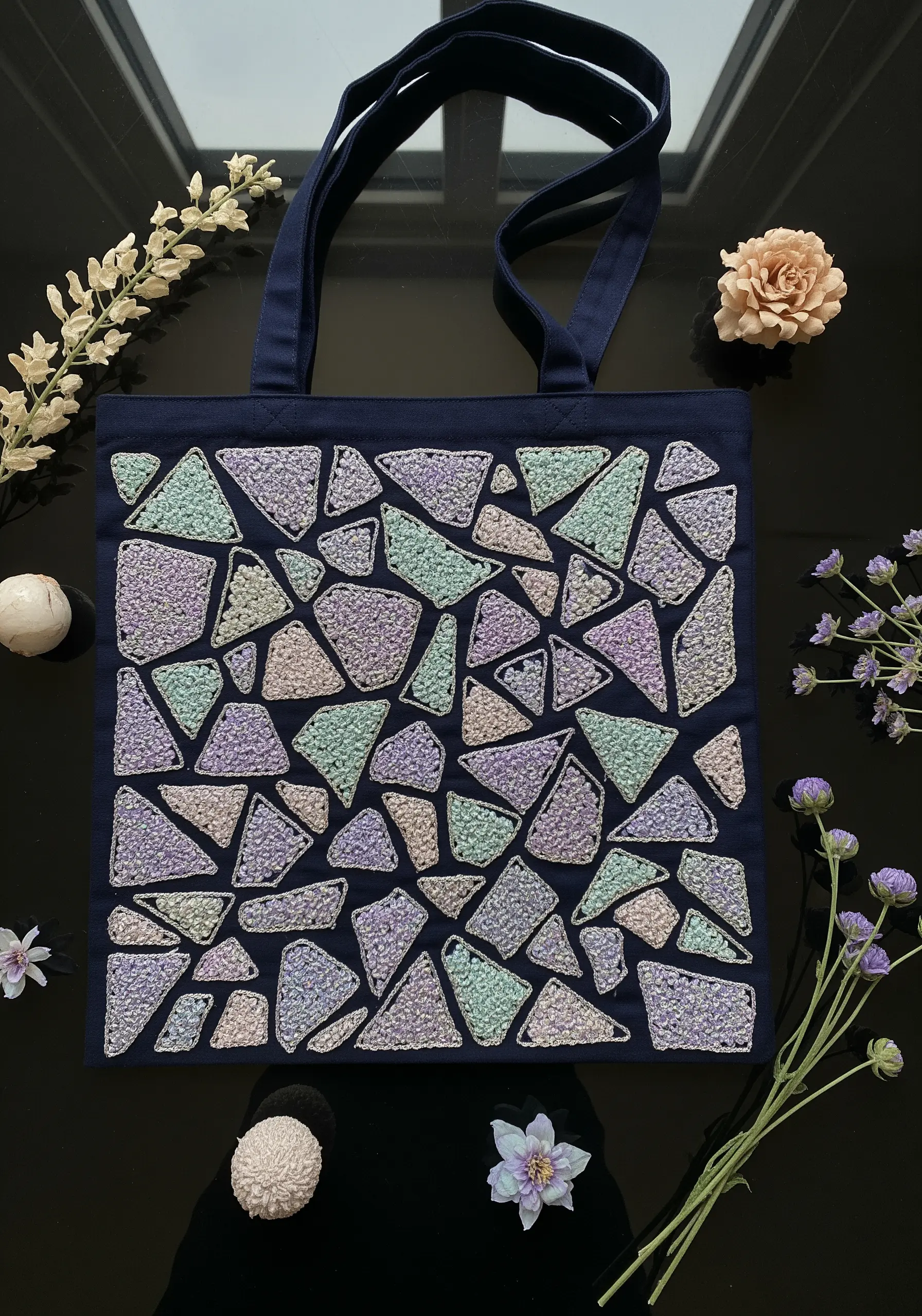 Abstract mosaic pattern in pastel tones, filled with textured French knots on a navy tote.