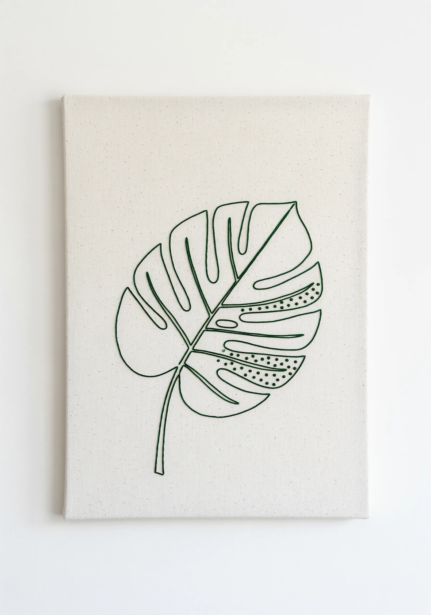 A single green embroidered line art monstera leaf on a plain canvas.