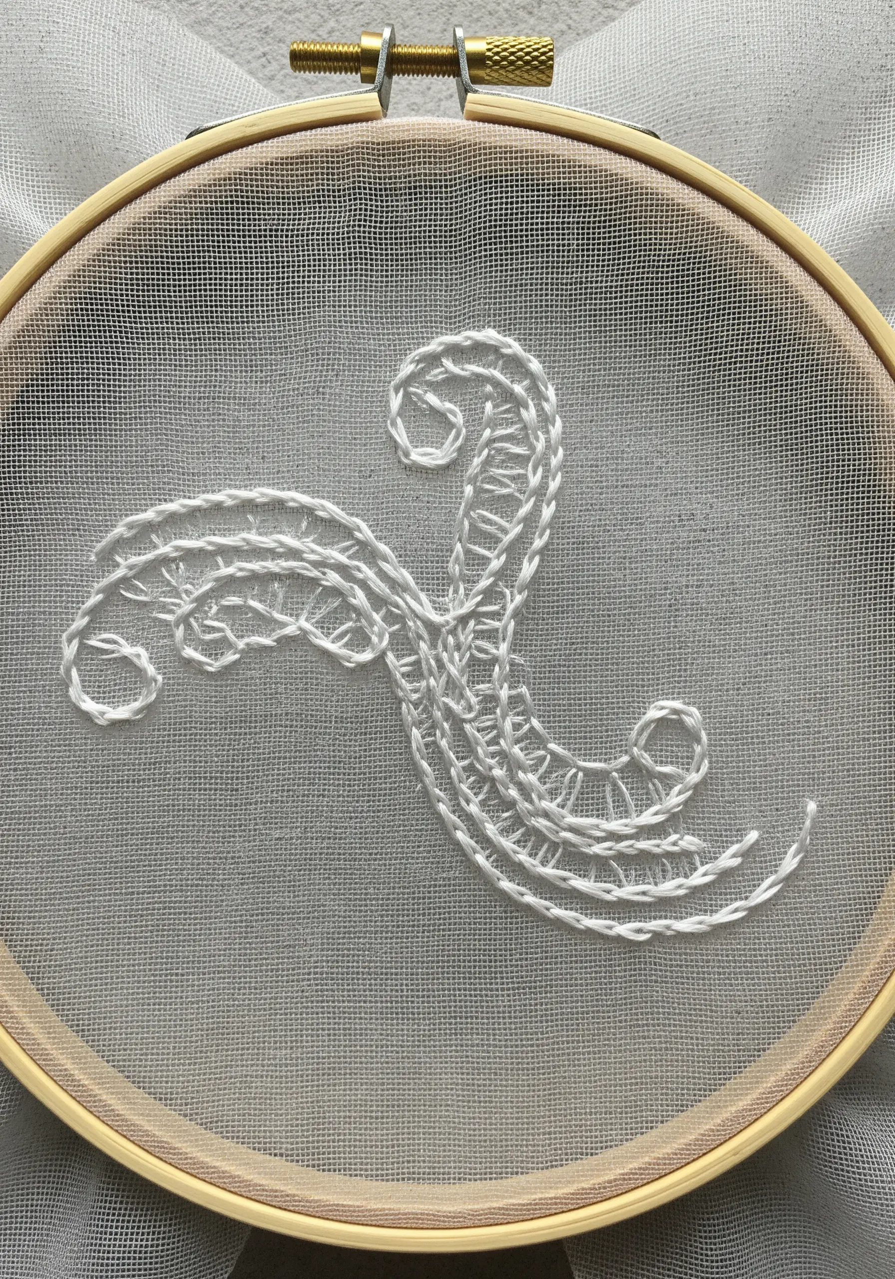 A delicate, abstract white embroidery on sheer, transparent fabric held in a hoop.