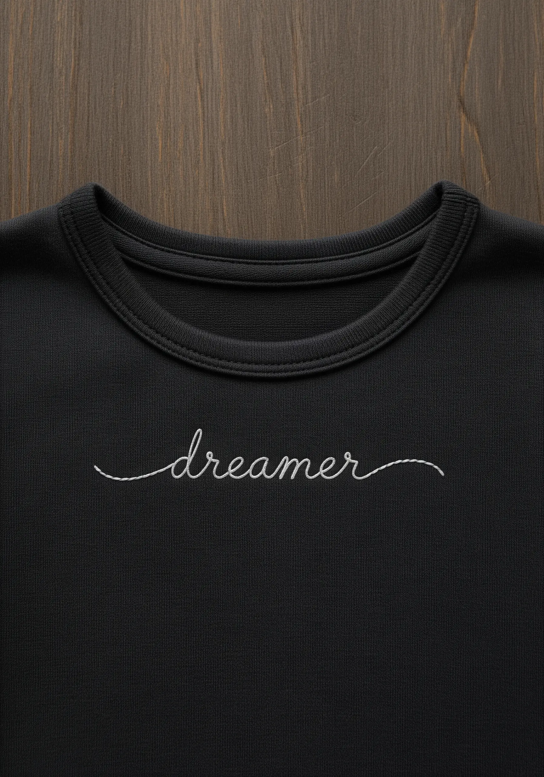 The word 'dreamer' embroidered in delicate white cursive script on a black sweatshirt.