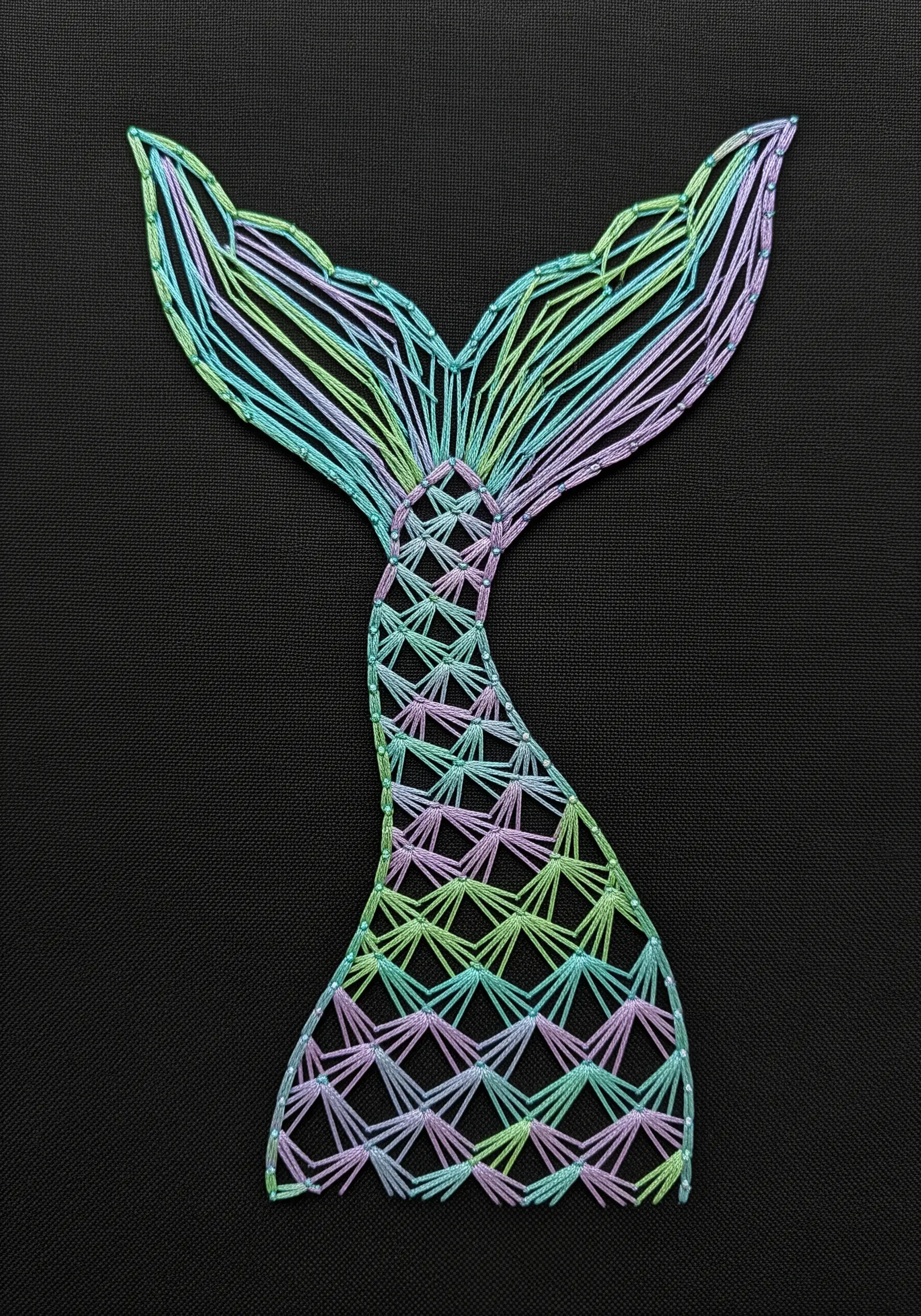 A mermaid tail with scales stitched in a shimmering, variegated metallic floss.