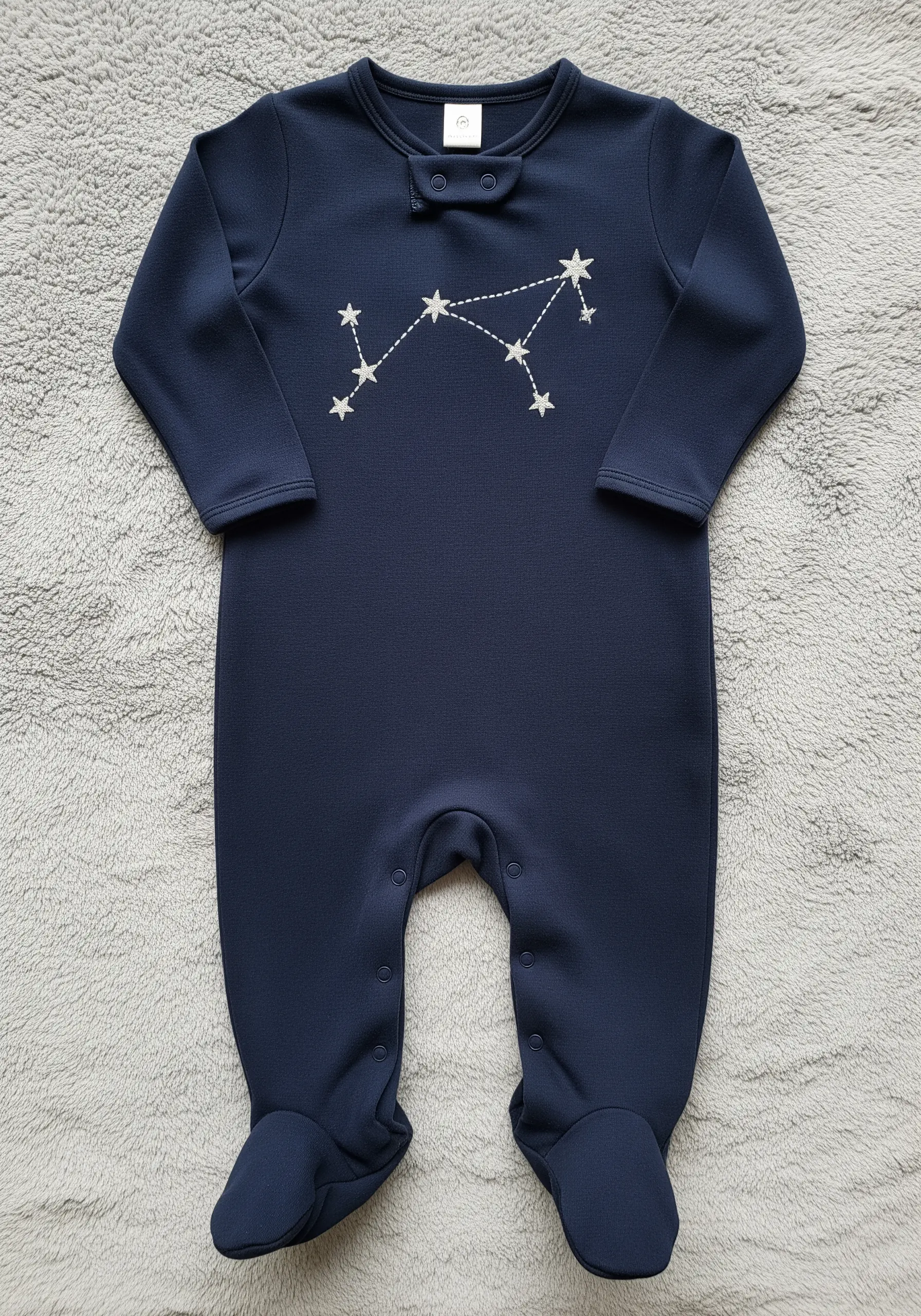 A zodiac constellation embroidered in white thread on a dark navy onesie.