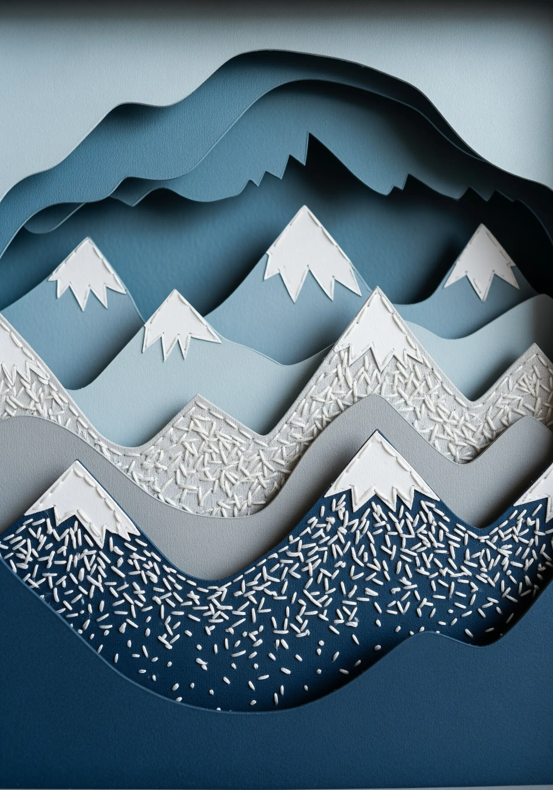 Layered paper mountains in shades of blue with scattered white seed stitches simulating snow.